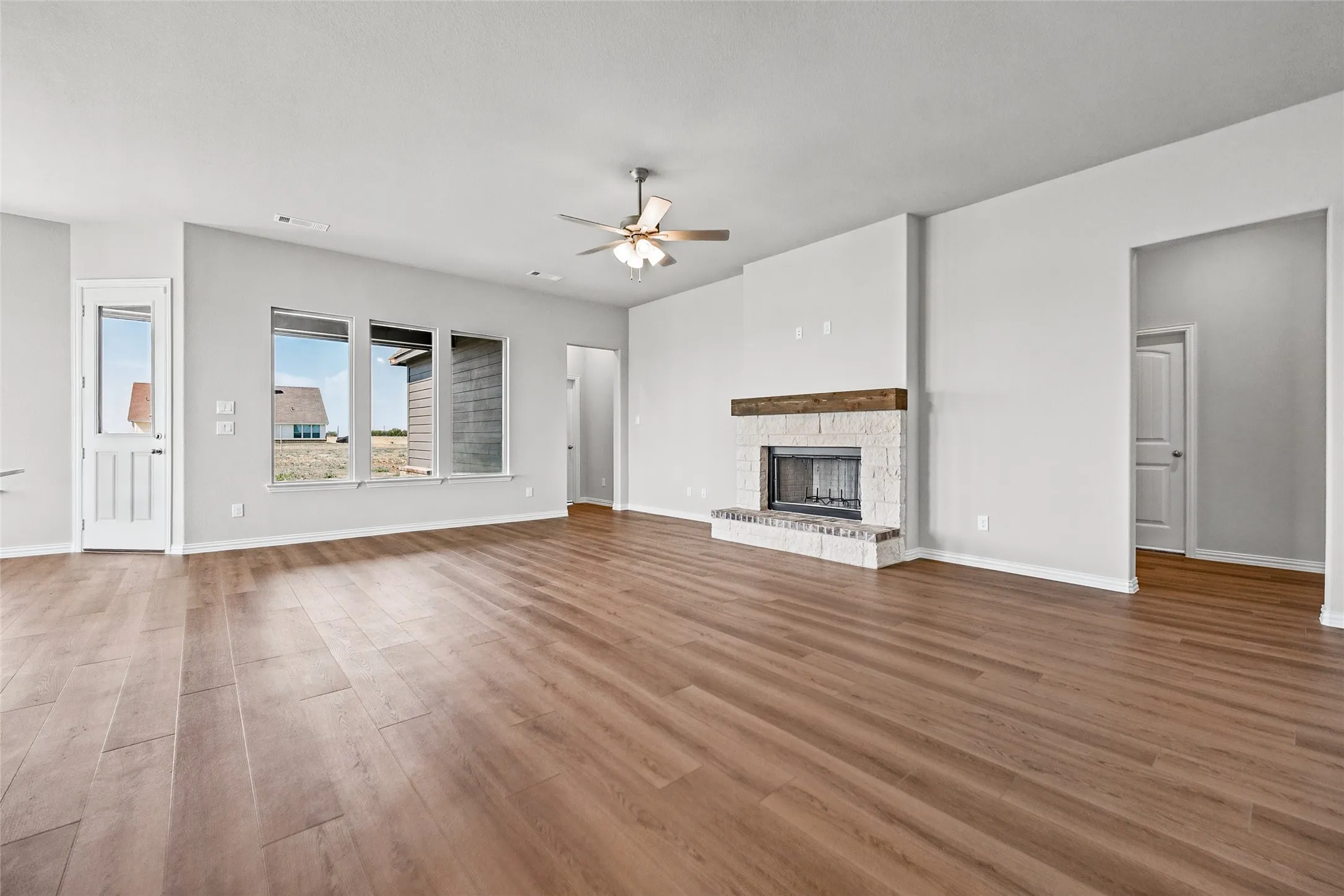 Wood-finish flooring throughout, a stone-clad fireplace with a wood mantle, and a ceiling fan with integrated lighting