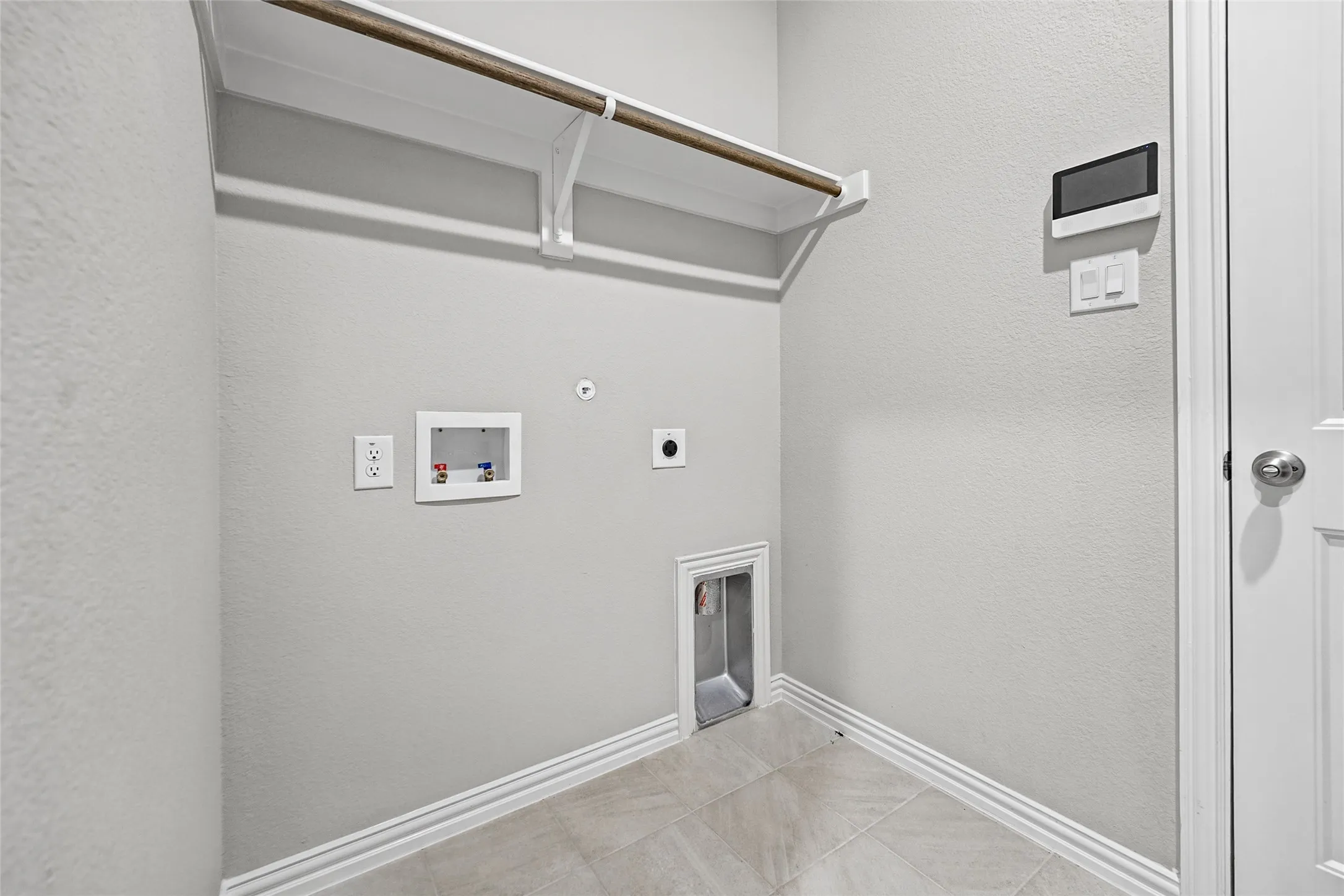 Laundry area with a built-in shelving unit, wood-finish hanging rod, utility hookups, and tiled flooring
