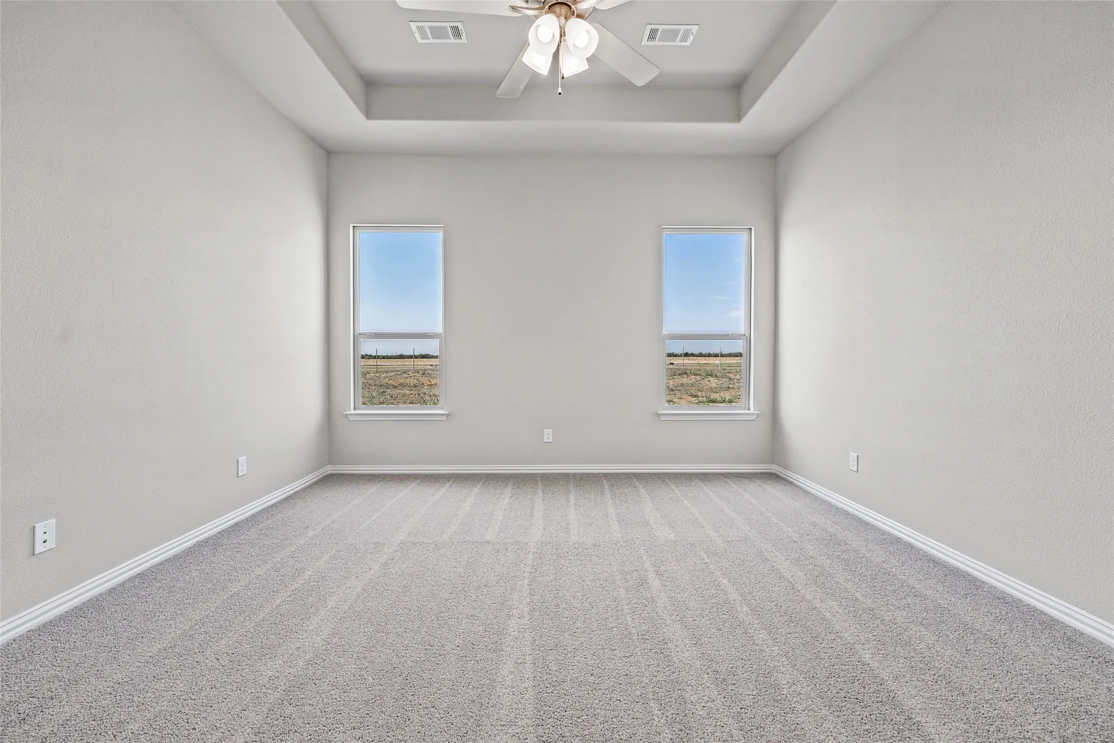 Tray ceiling with a ceiling fan, two windows, and light gray carpeting