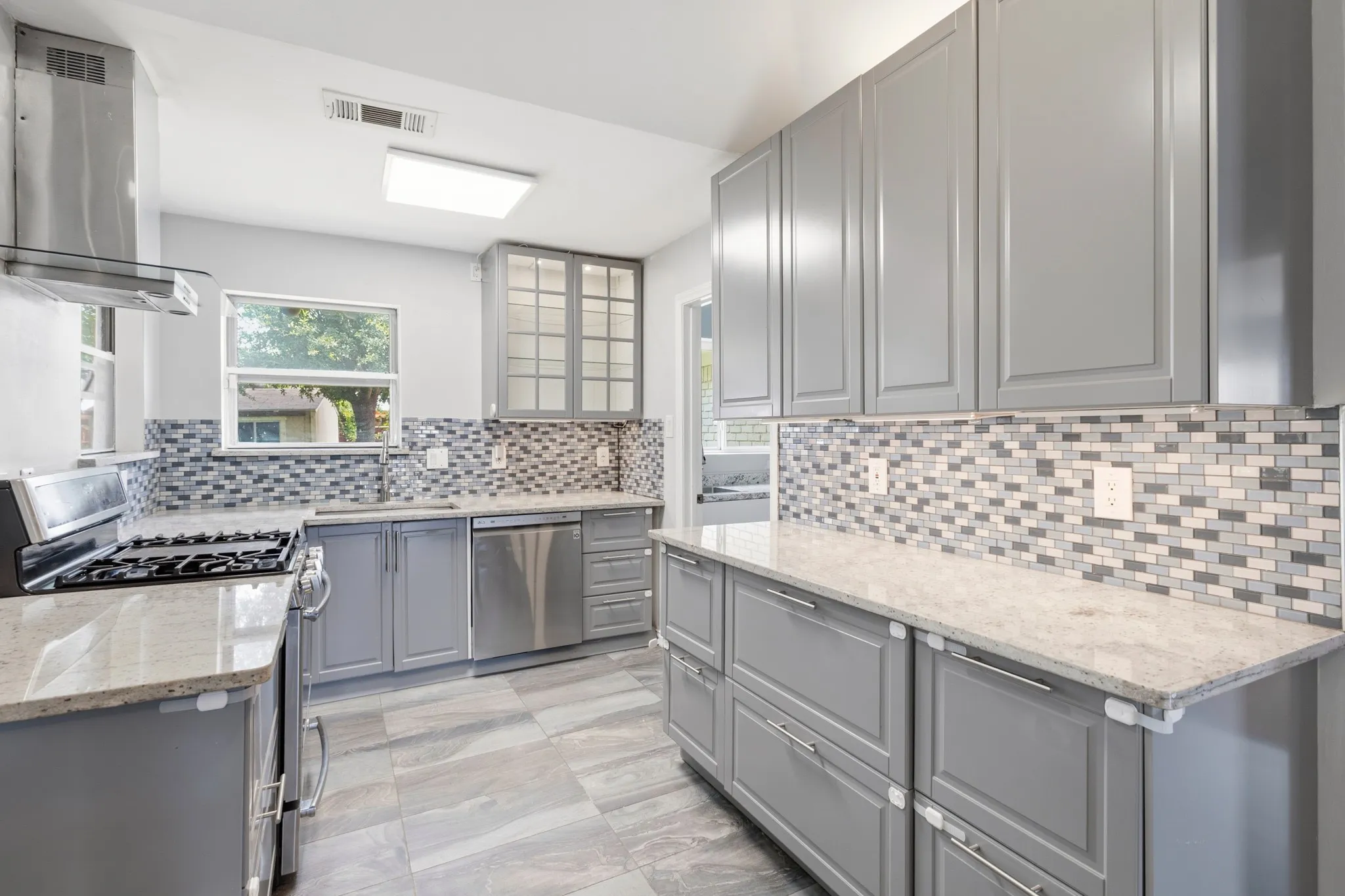 Kitchen featuring contemporary gray cabinetry, light-toned countertops, and a mosaic tile backsplash