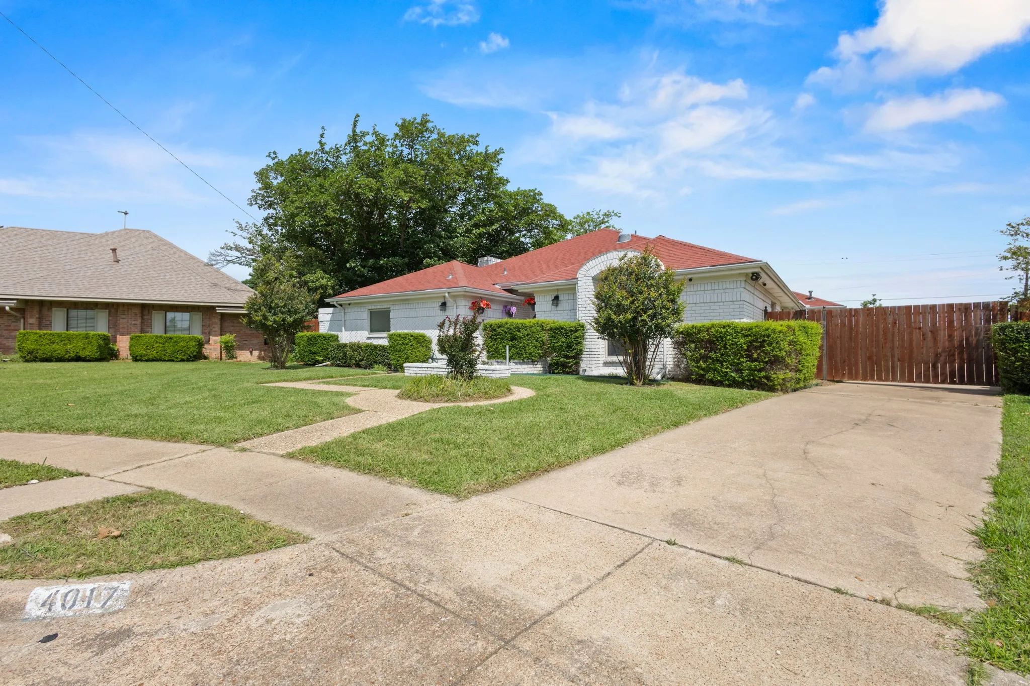 Exterior featuring a red roof, white siding, manicured front lawn, concrete driveway, and a privacy fence