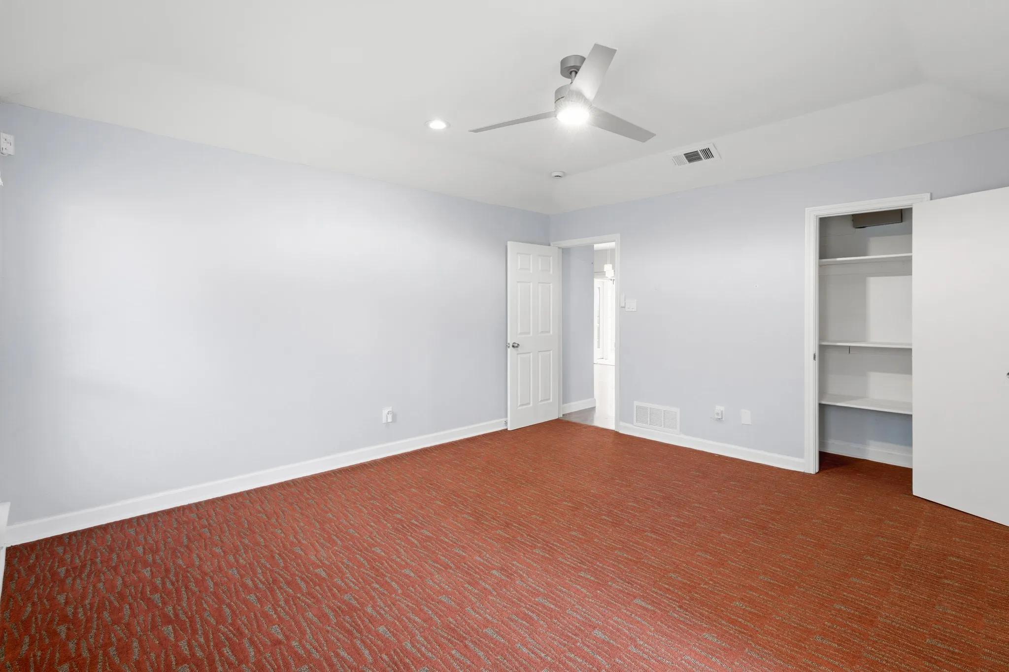 Spacious room featuring patterned red-brown carpeting, light-toned walls, and a modern ceiling fan with integrated lighting