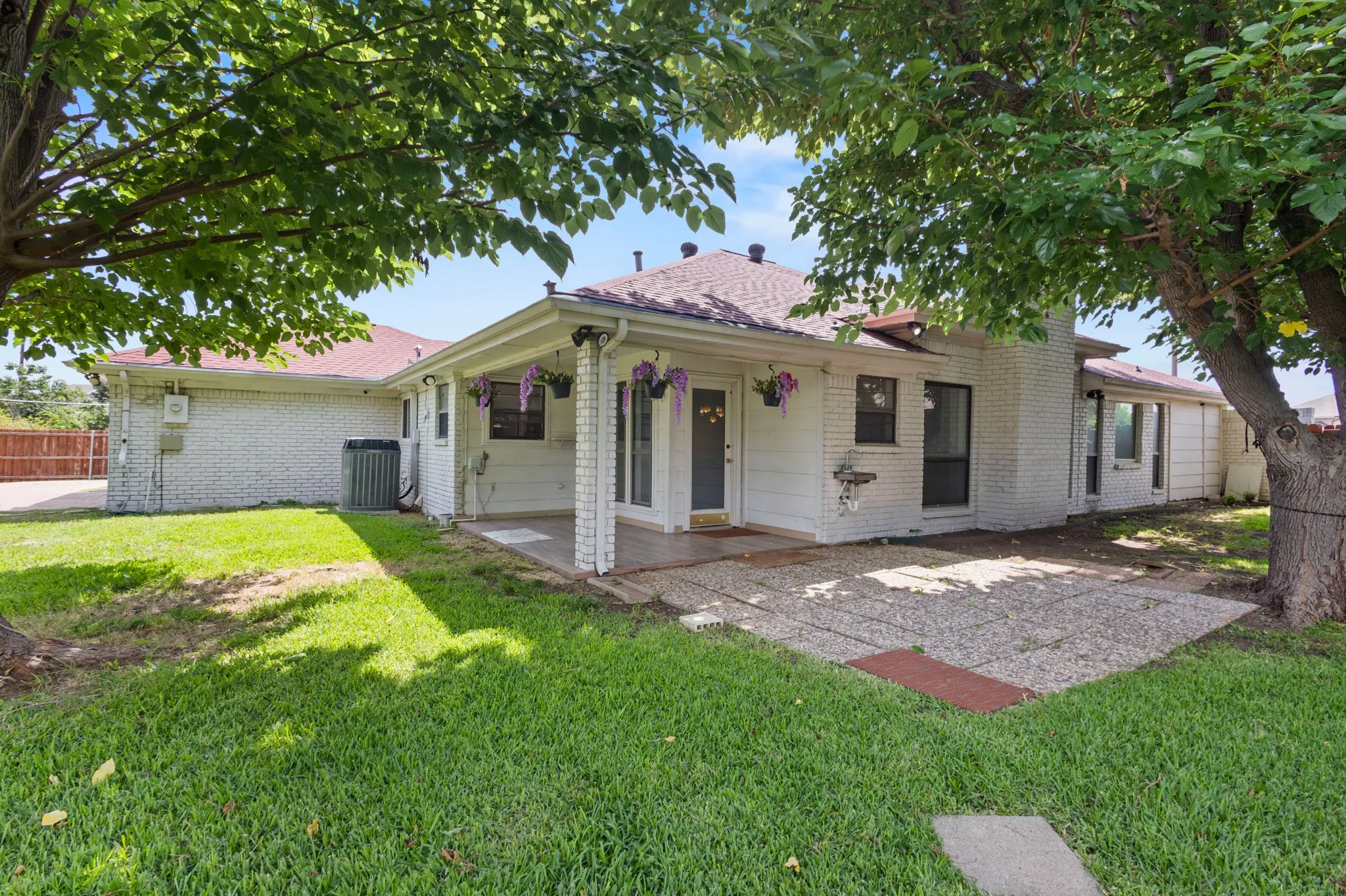 Expansive grassy backyard featuring mature trees, stepping stones, and a covered patio area