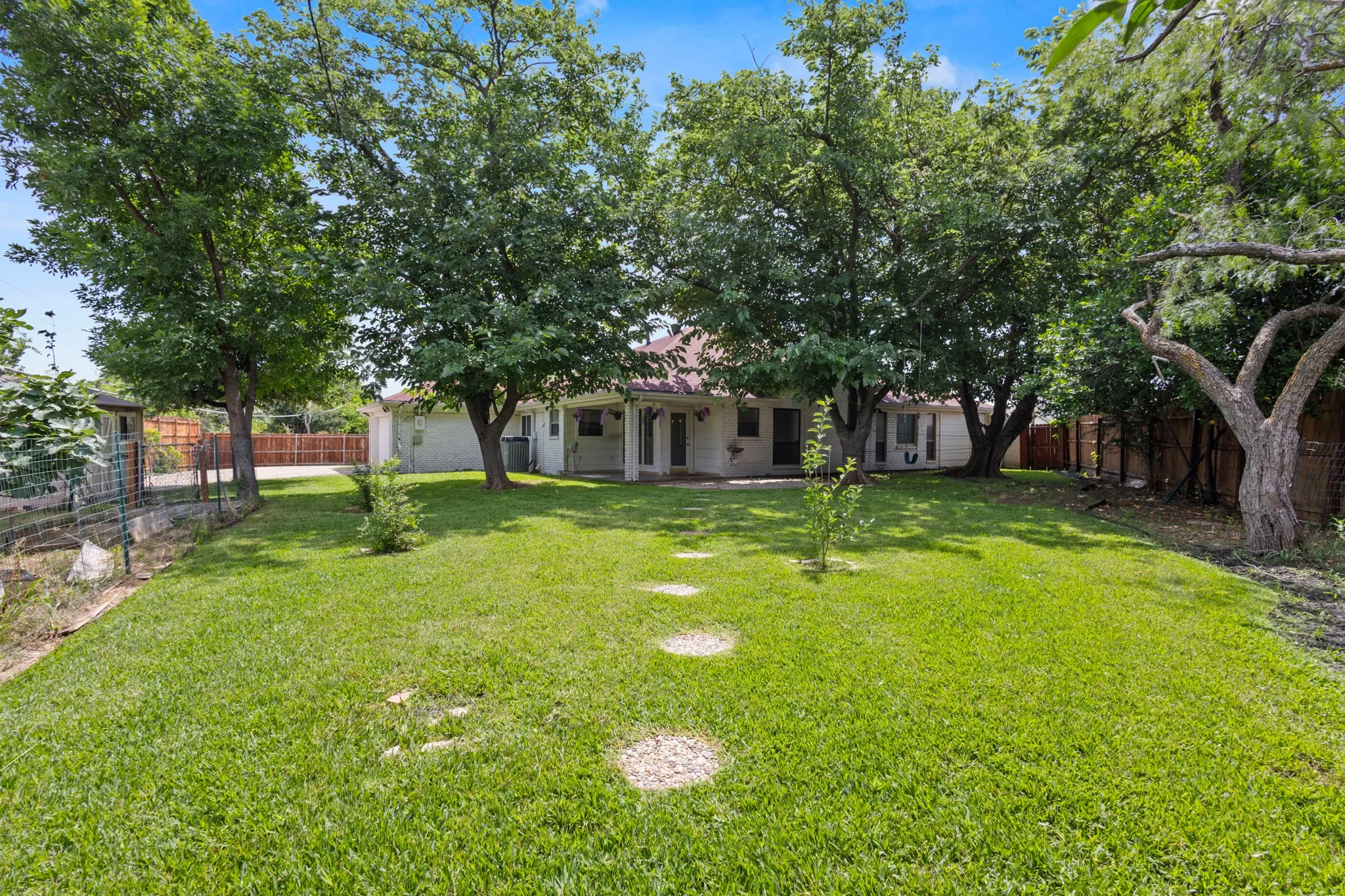 Expansive grassy backyard featuring mature trees, stepping stones, and a covered patio area