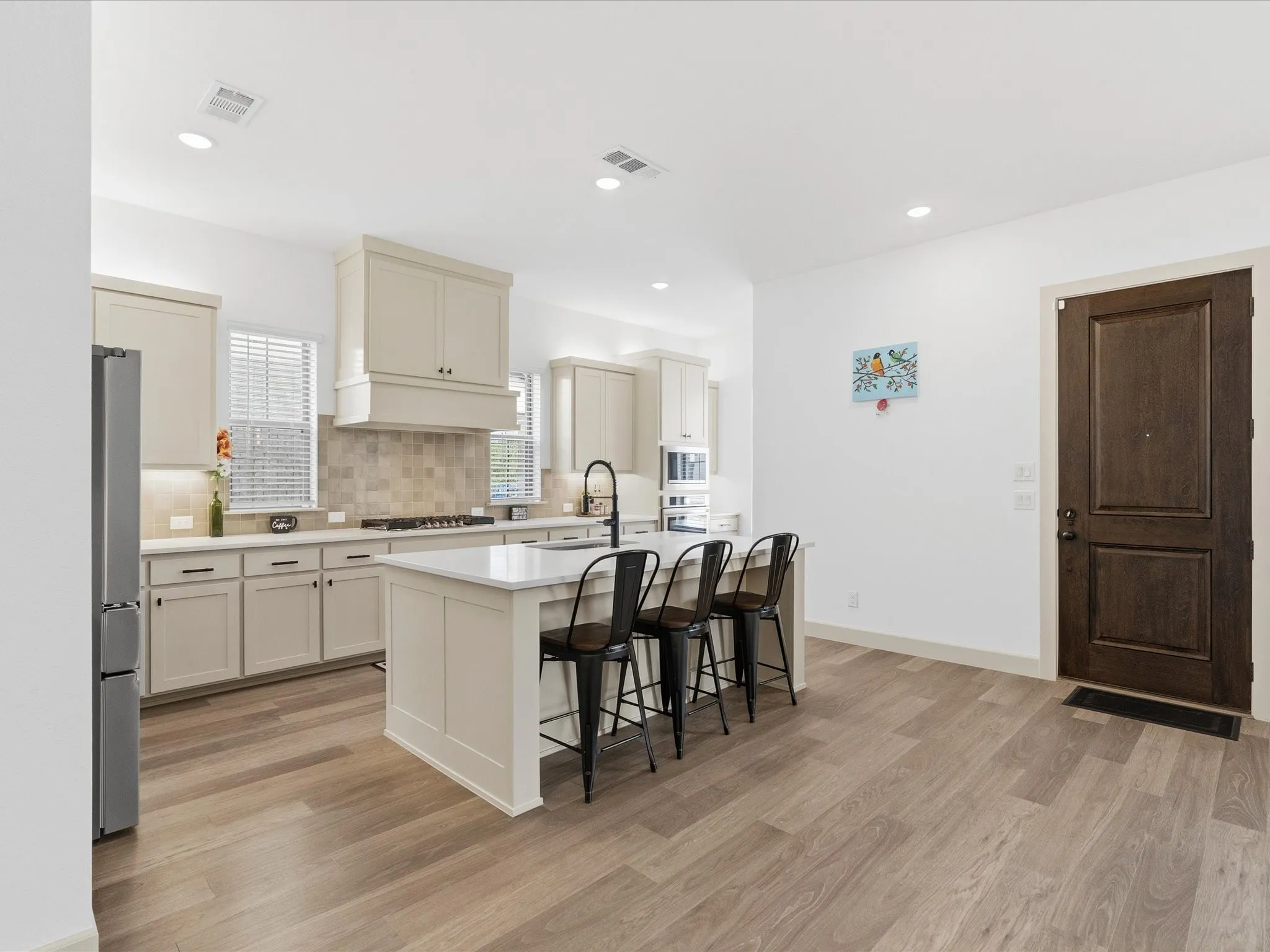 Spacious kitchen featuring a central island with countertop seating, light-toned cabinetry, light wood-finish flooring, recessed lighting, and a tile backsplash