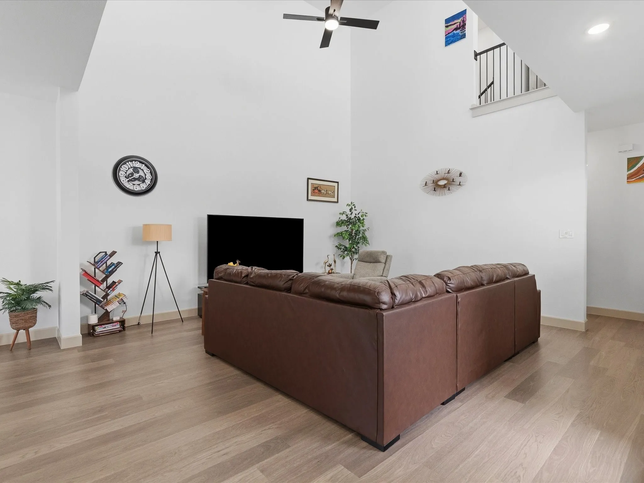 Spacious living area featuring a vaulted ceiling, ceiling fan, wood-finish flooring, white walls, and a staircase with black metal balusters
