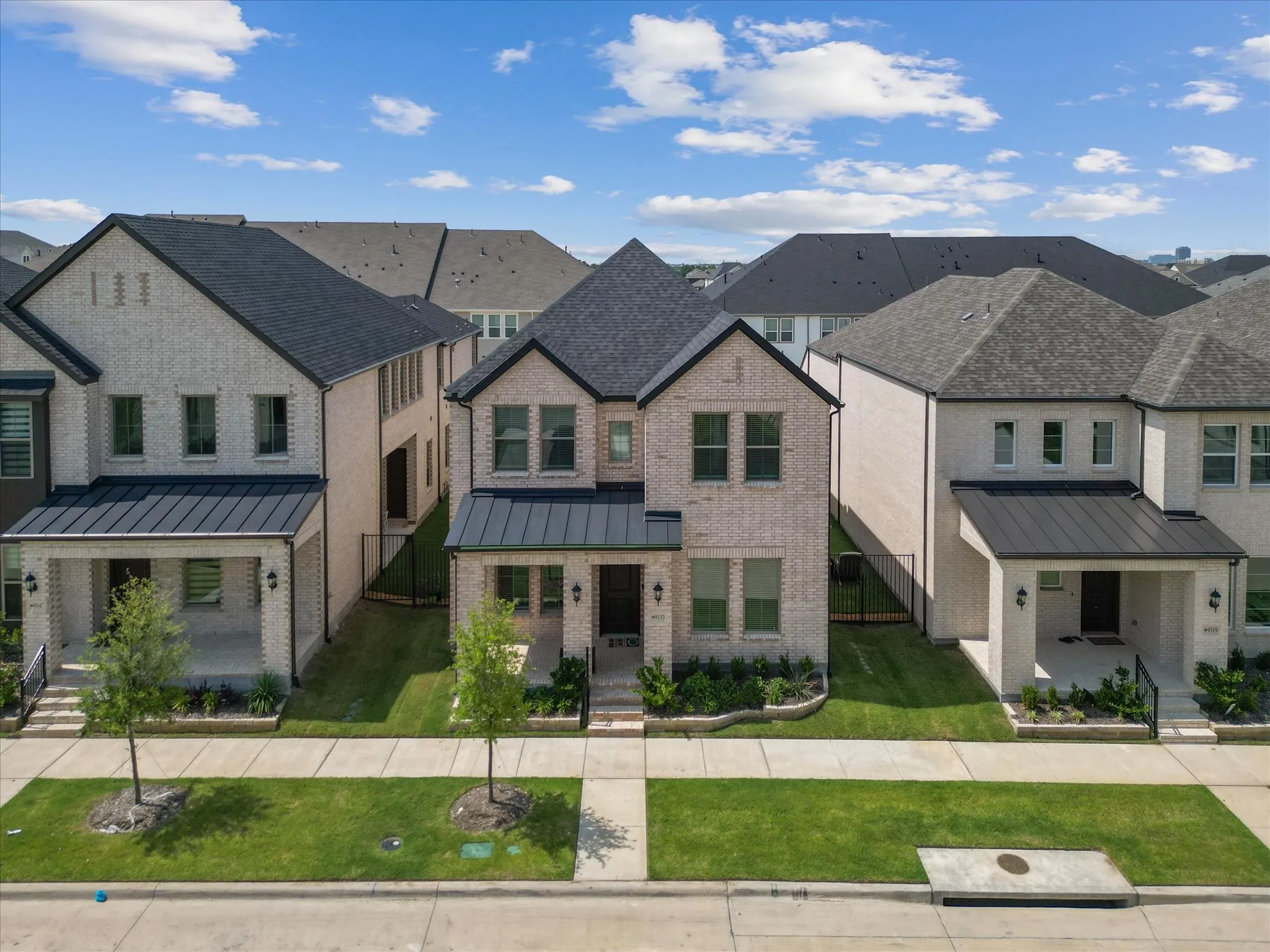 Two-story brick exterior featuring a black shingle roof, dark metal awnings, a covered front porch, and manicured front landscaping