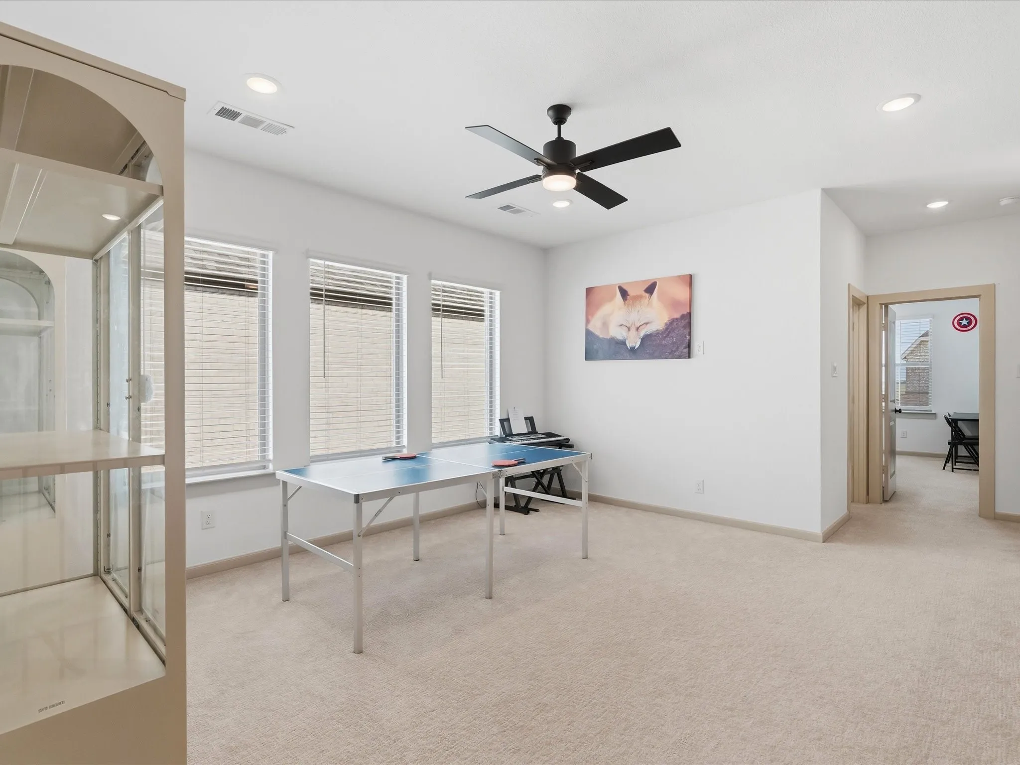 Spacious room featuring neutral carpet flooring, three large windows with blinds, a ceiling fan, and recessed lighting