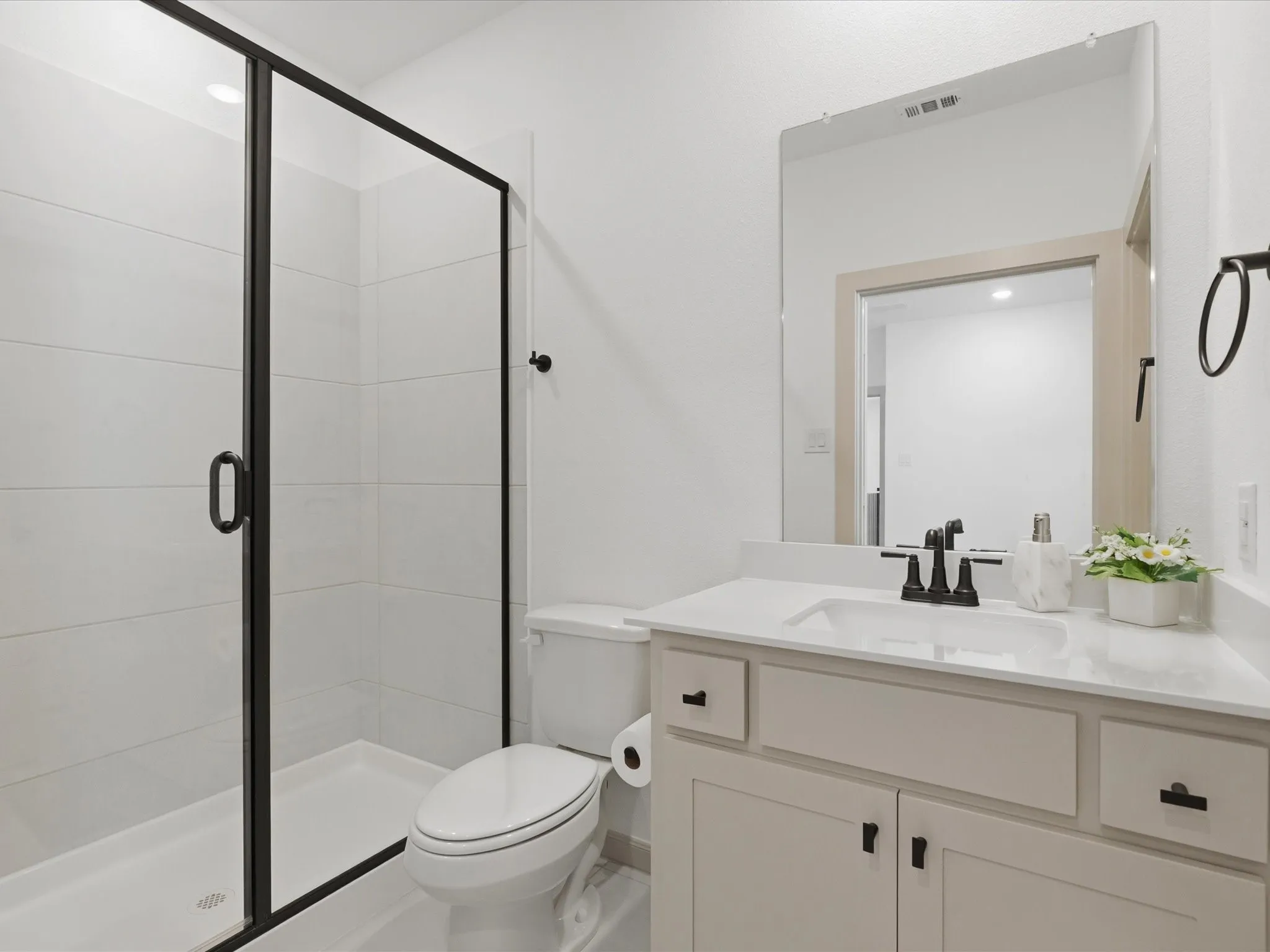 Bathroom featuring a glass-enclosed shower with black trim, a white vanity with an integrated sink, a large wall-mounted mirror, and black fixtures