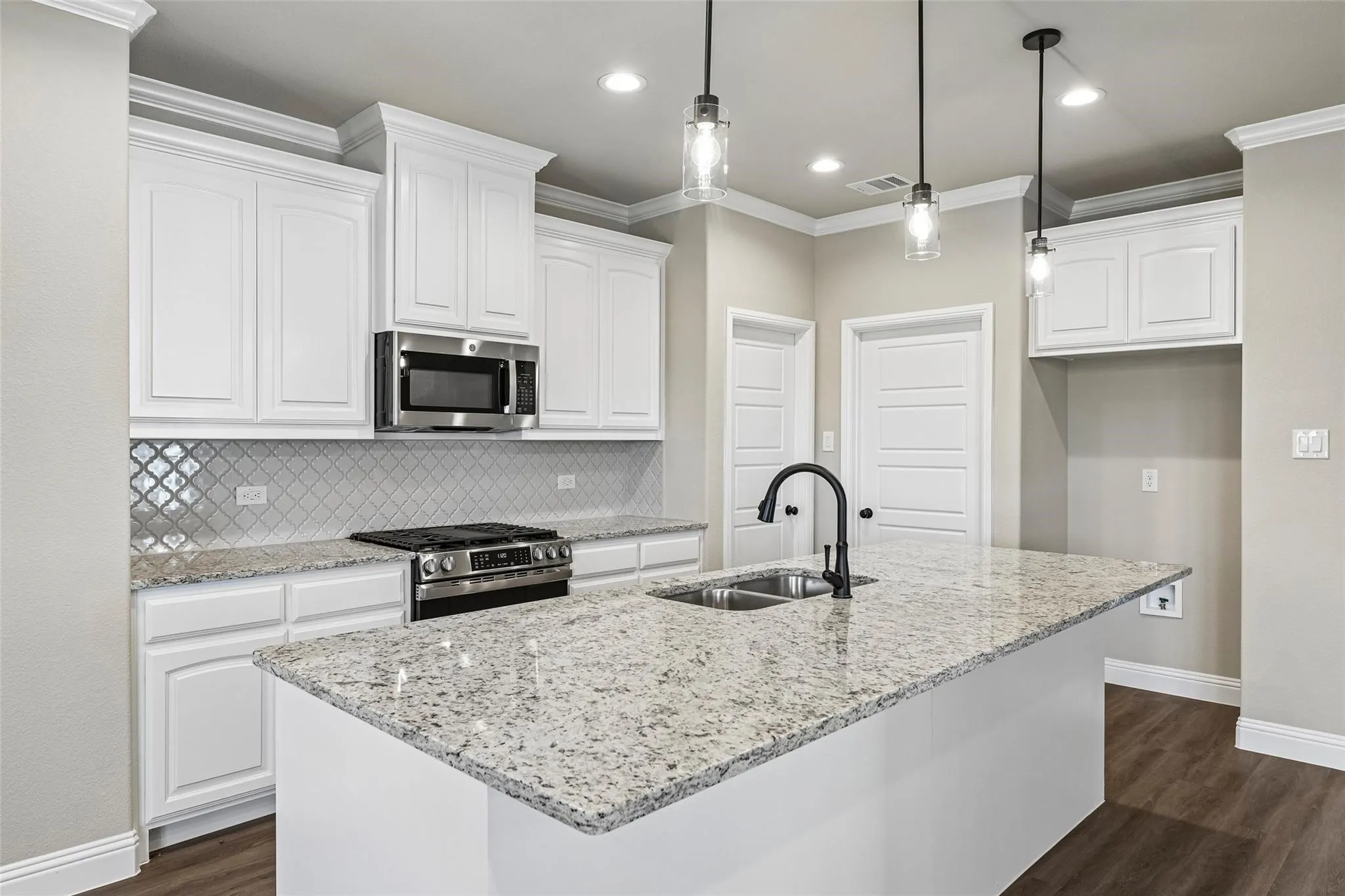 Modern kitchen featuring white cabinetry, a granite-topped island with seating space, stainless steel gas range, and pendant lighting