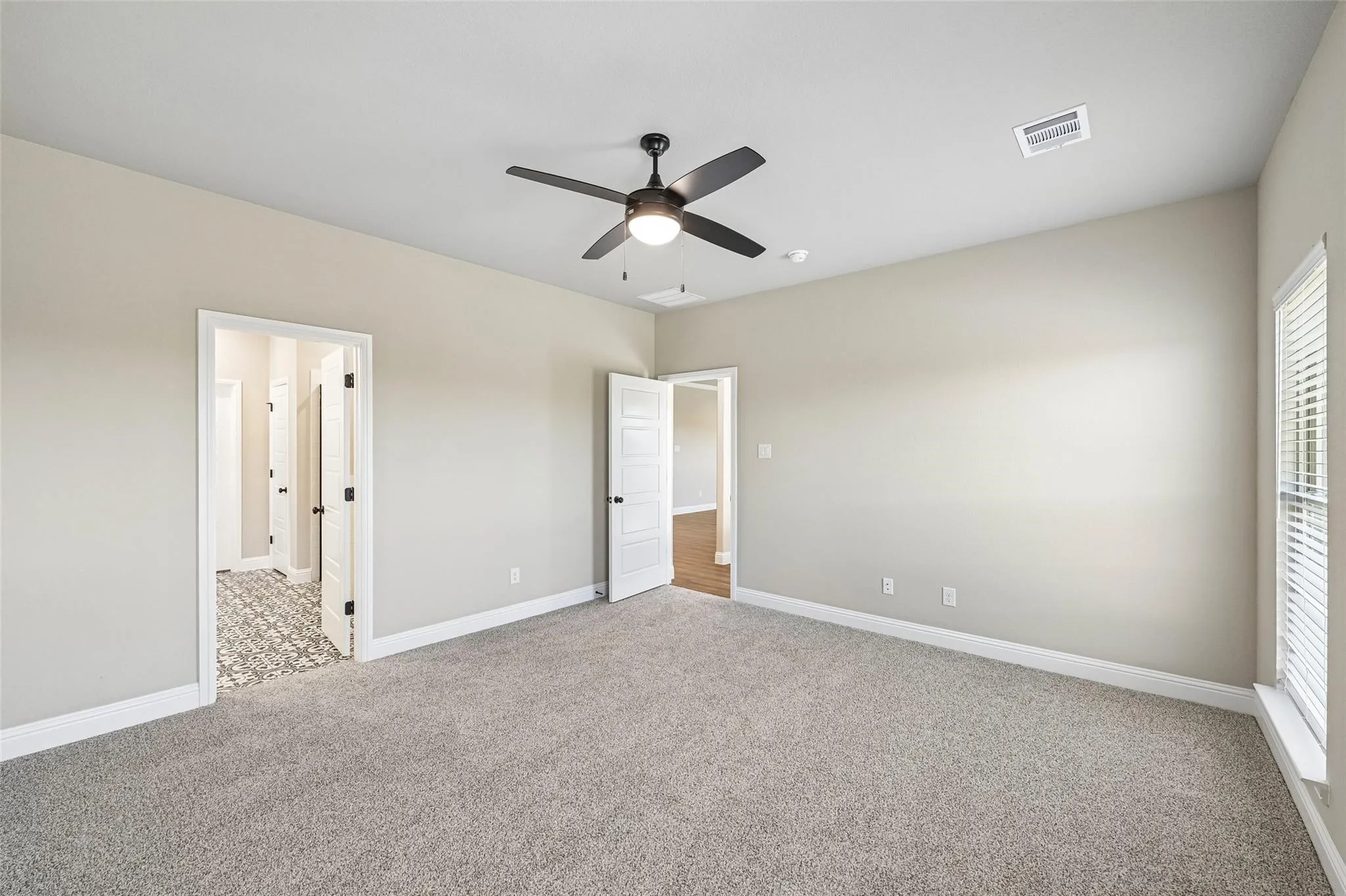 Spacious carpeted room featuring a ceiling fan, neutral wall tones, and multiple doorways