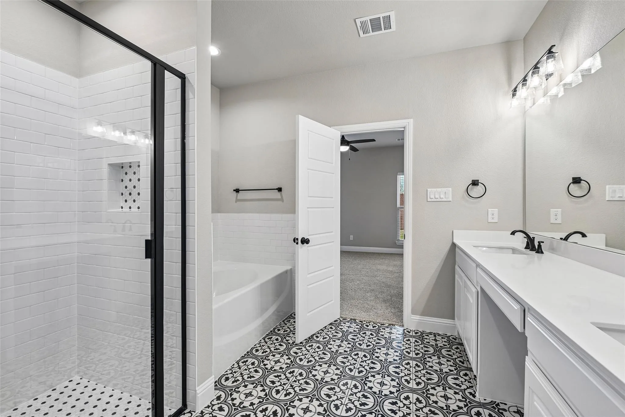 Black-framed glass shower with white subway tile surround, a built-in tub, dual vanity with undermount sinks, and patterned floor tile
