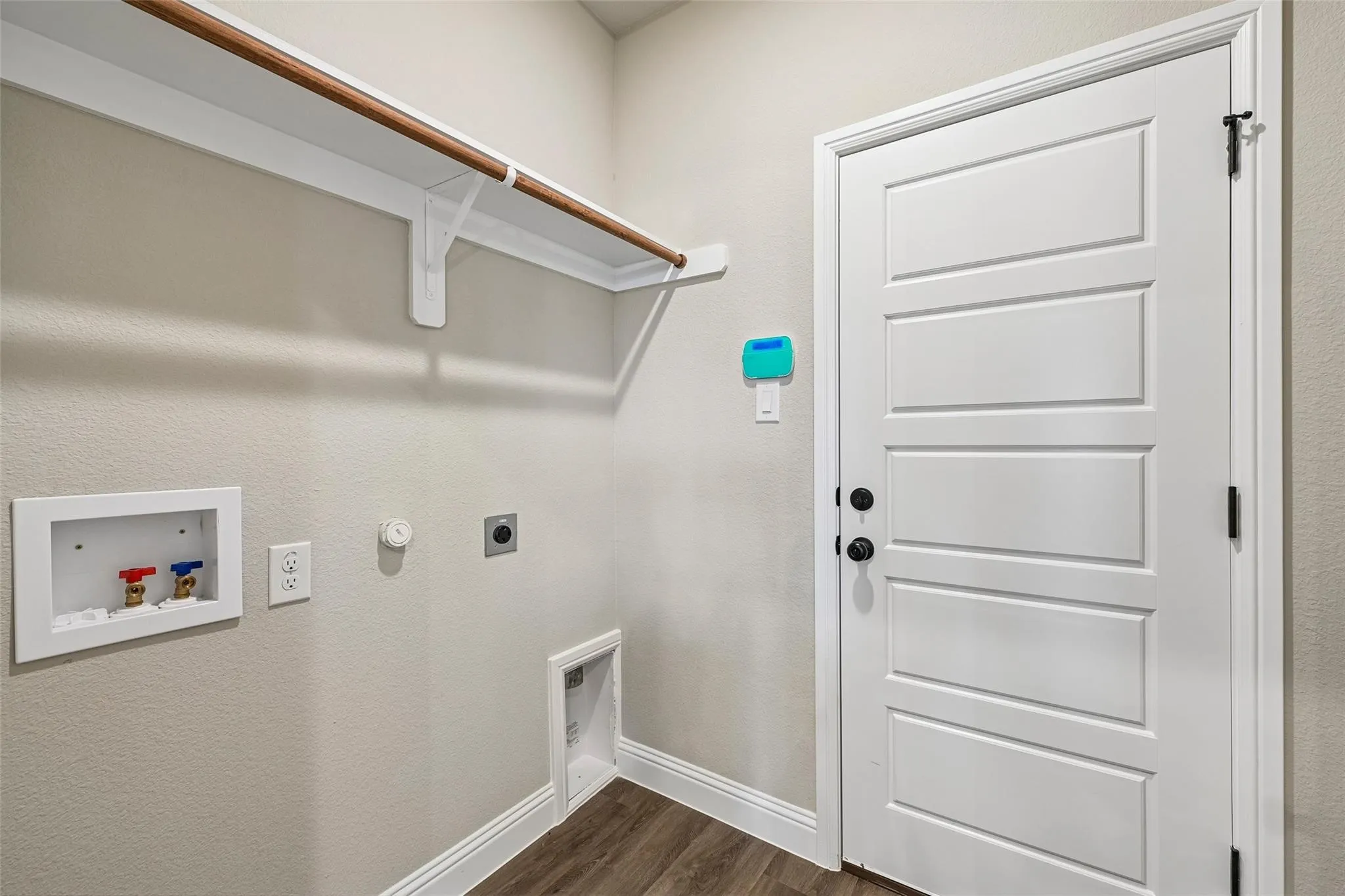 Dedicated utility space featuring wood-finish flooring, a built-in hanging rod, and a panel door