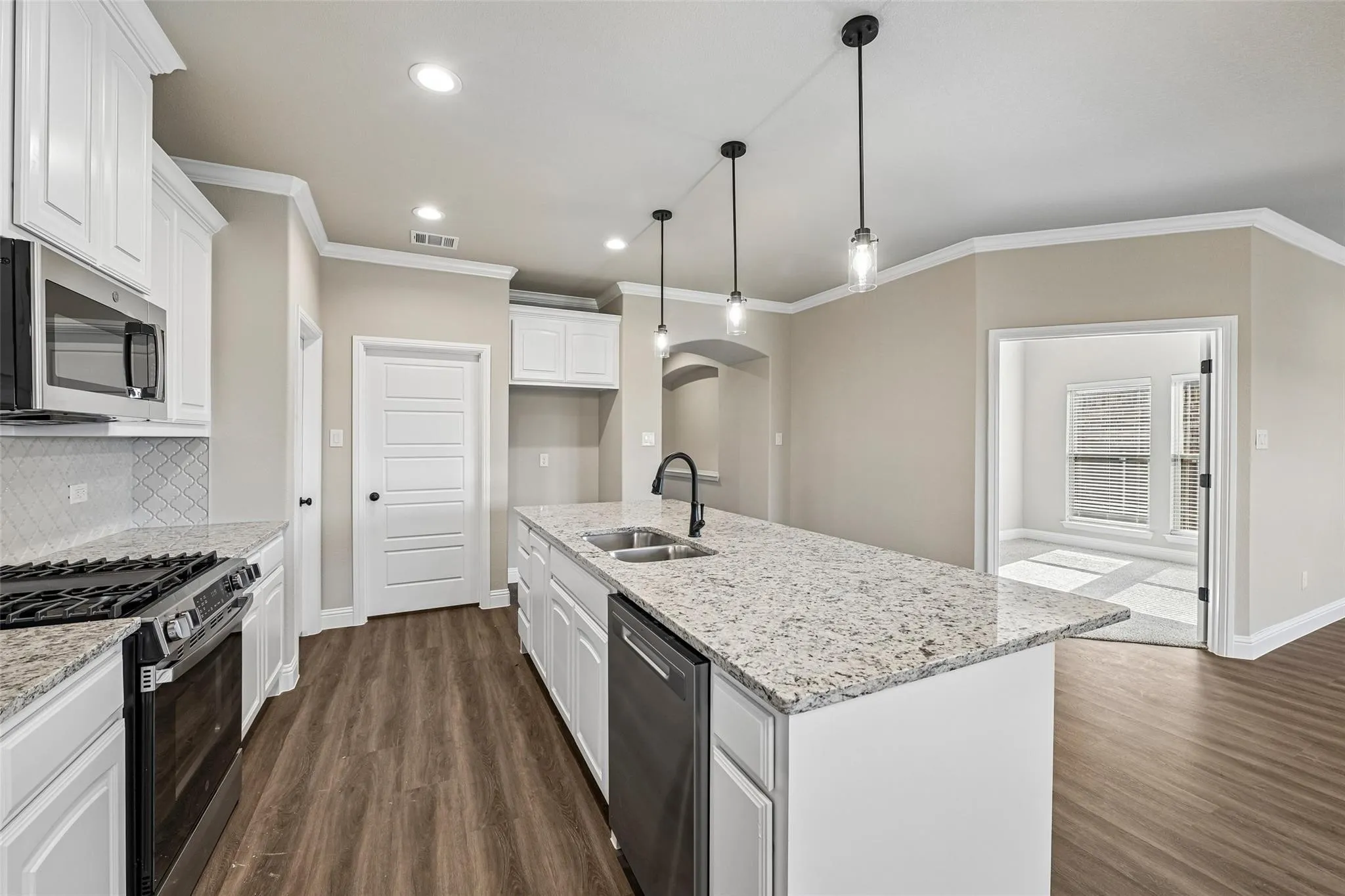 Kitchen featuring an expansive island with a dual sink, pendant lighting, built-in microwave, white shaker-style cabinetry, and wood-finish flooring