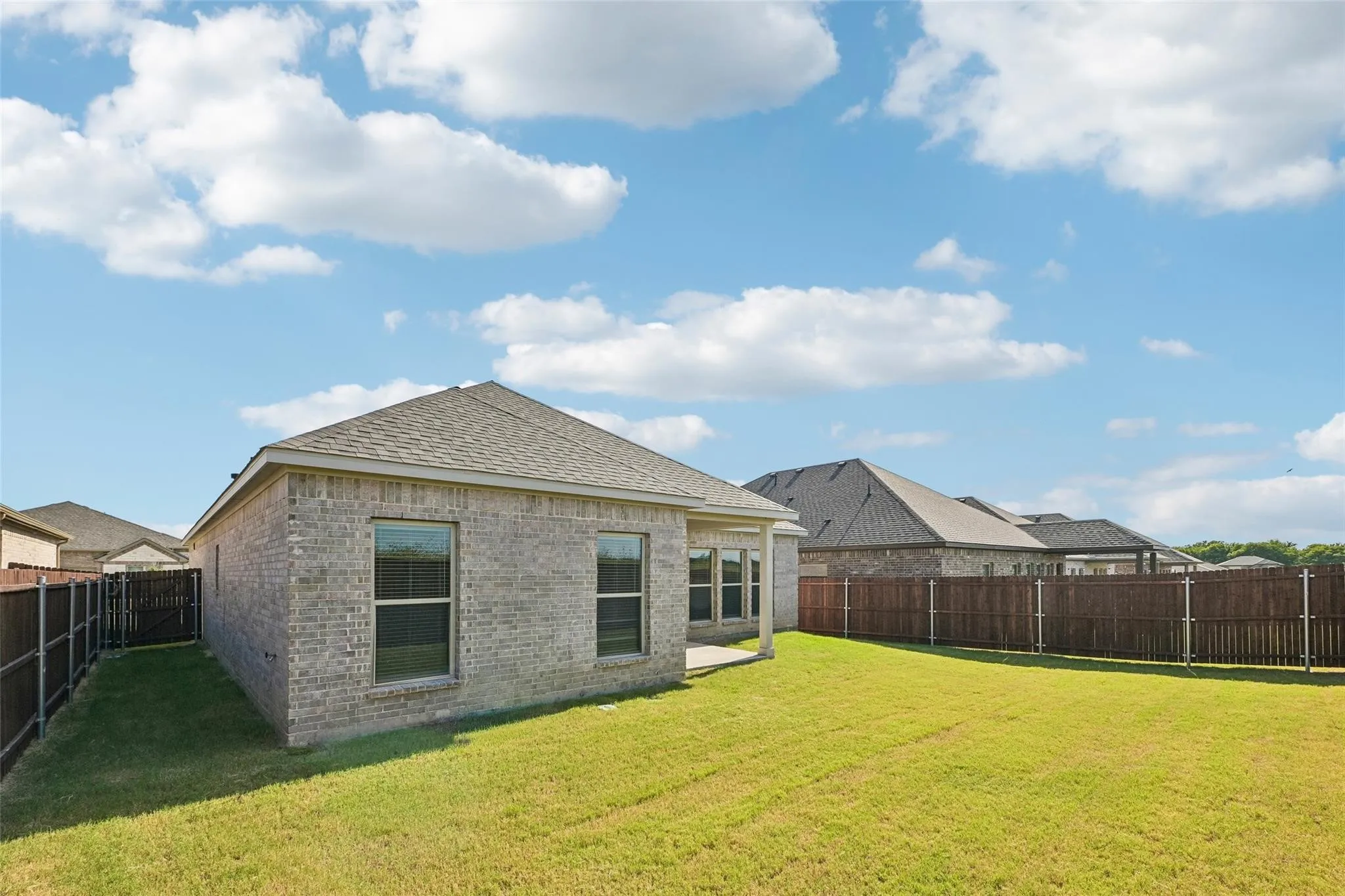 Expansive backyard with a manicured lawn, full perimeter fencing, brick exterior, covered patio, and dual-pane windows