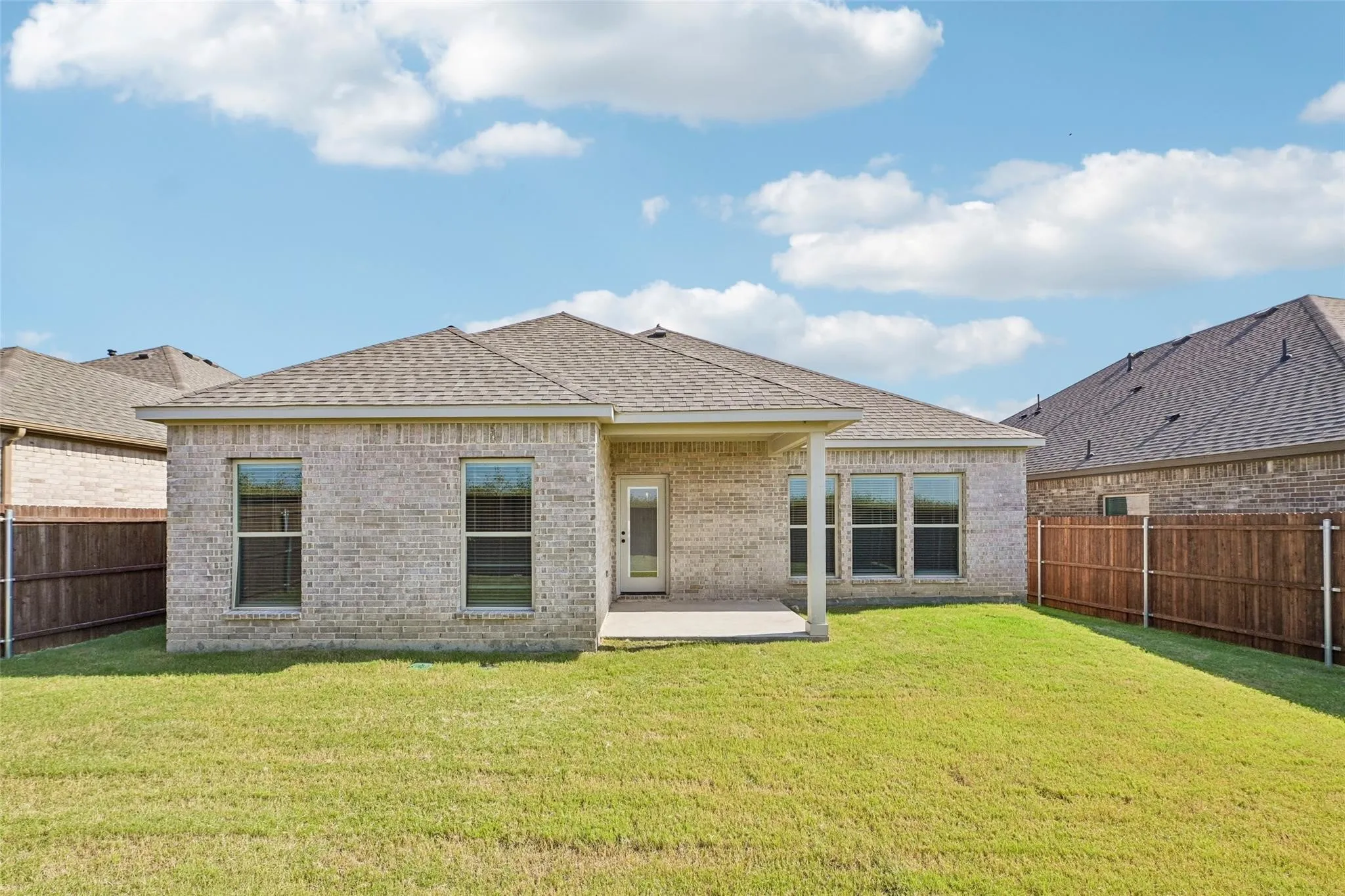 Rear exterior featuring a covered patio, brick facade, shingle roof, and a fenced yard