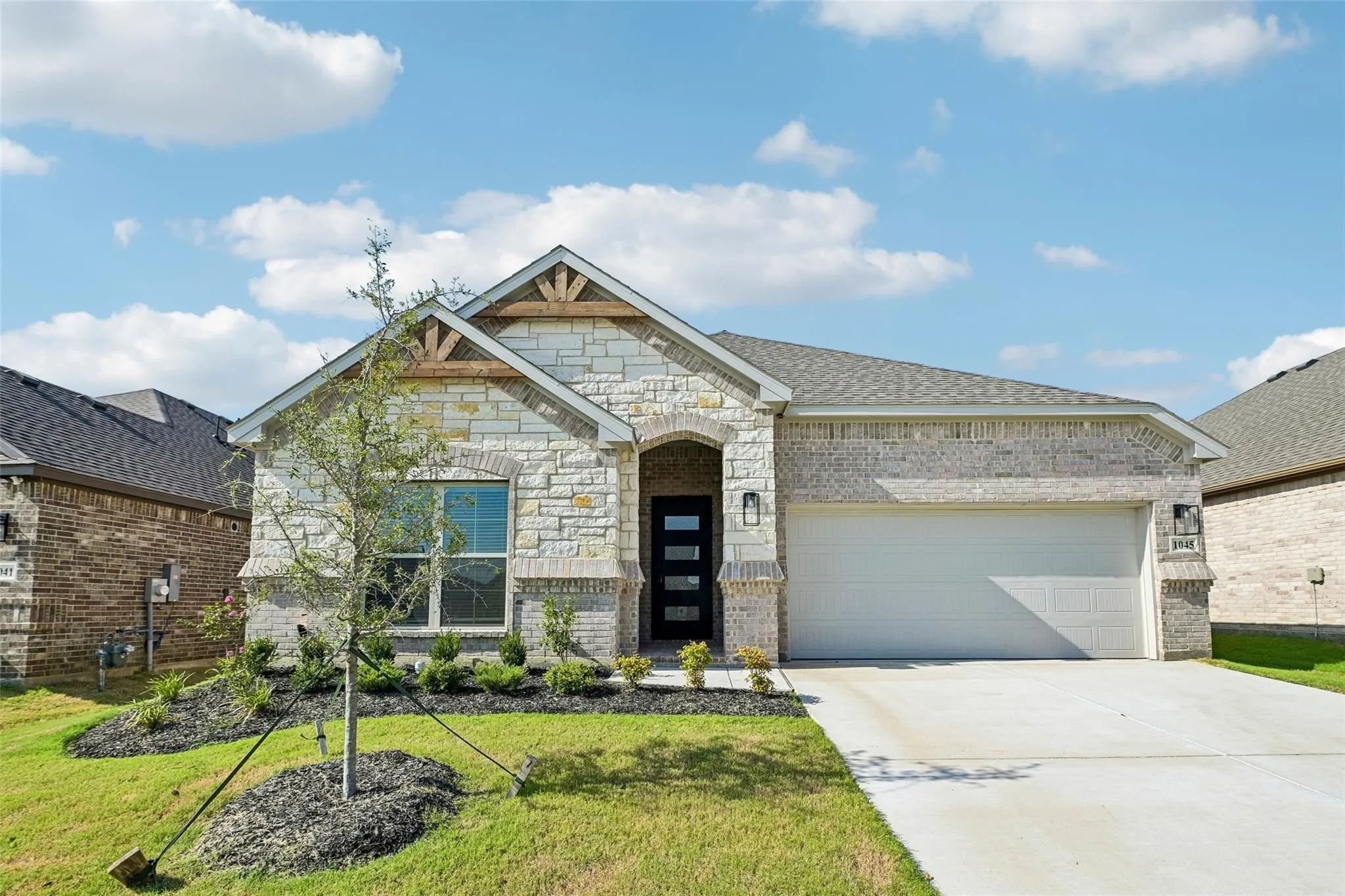 Stone and brick facade with wood accents, a two-car garage, and a concrete driveway