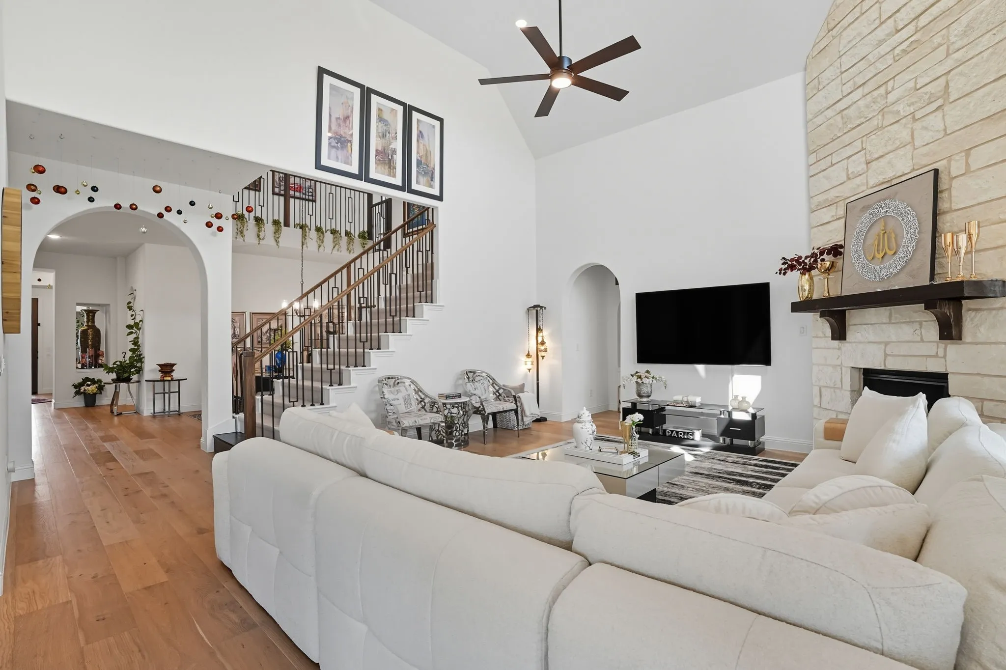 Great room featuring a vaulted ceiling with a contemporary ceiling fan, a fireplace with a stone surround and wood mantel, wood-finish flooring, and an arched entry