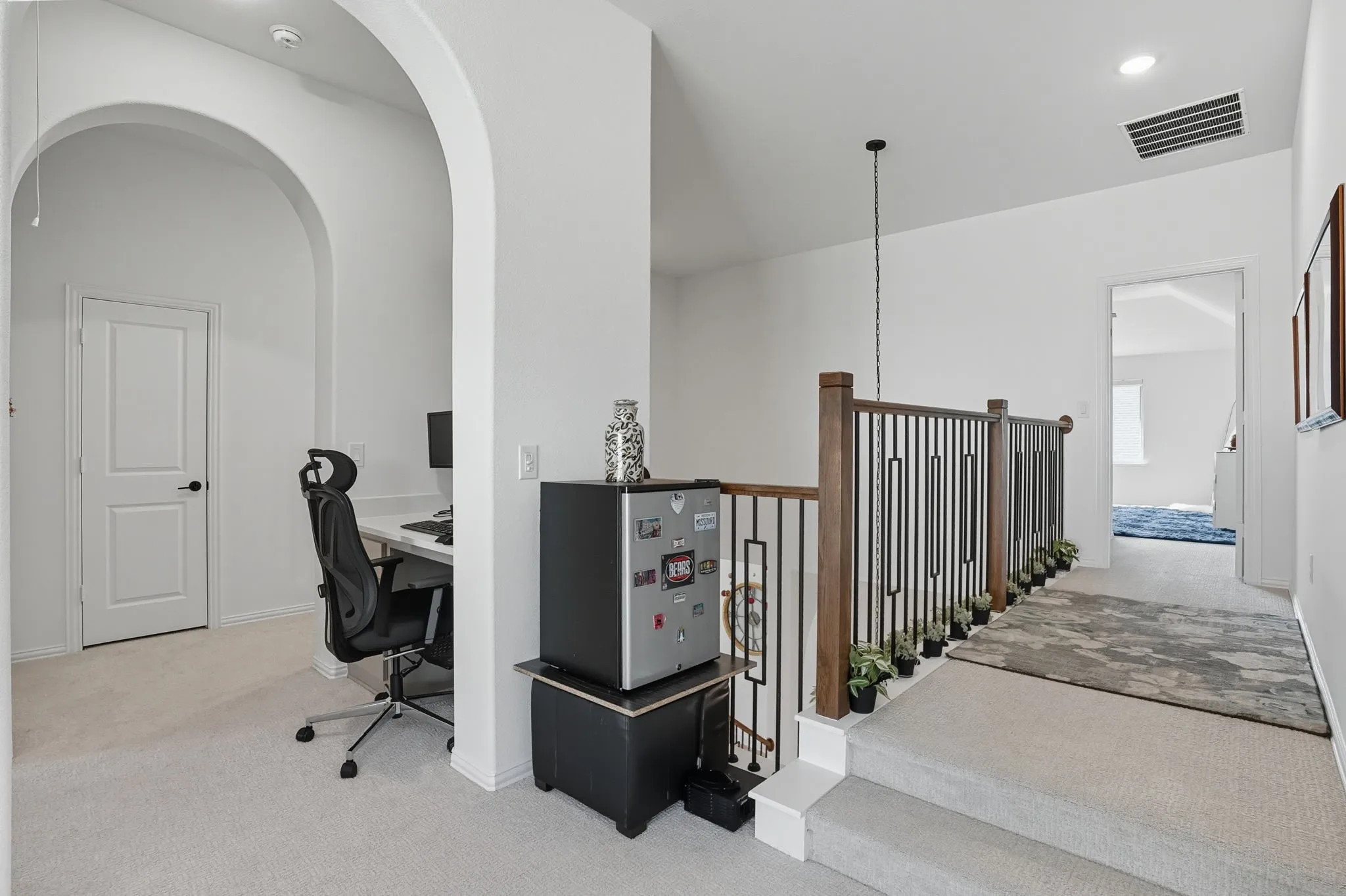 Carpeted landing featuring a wood and iron baluster railing system, arched doorway, and recessed lighting