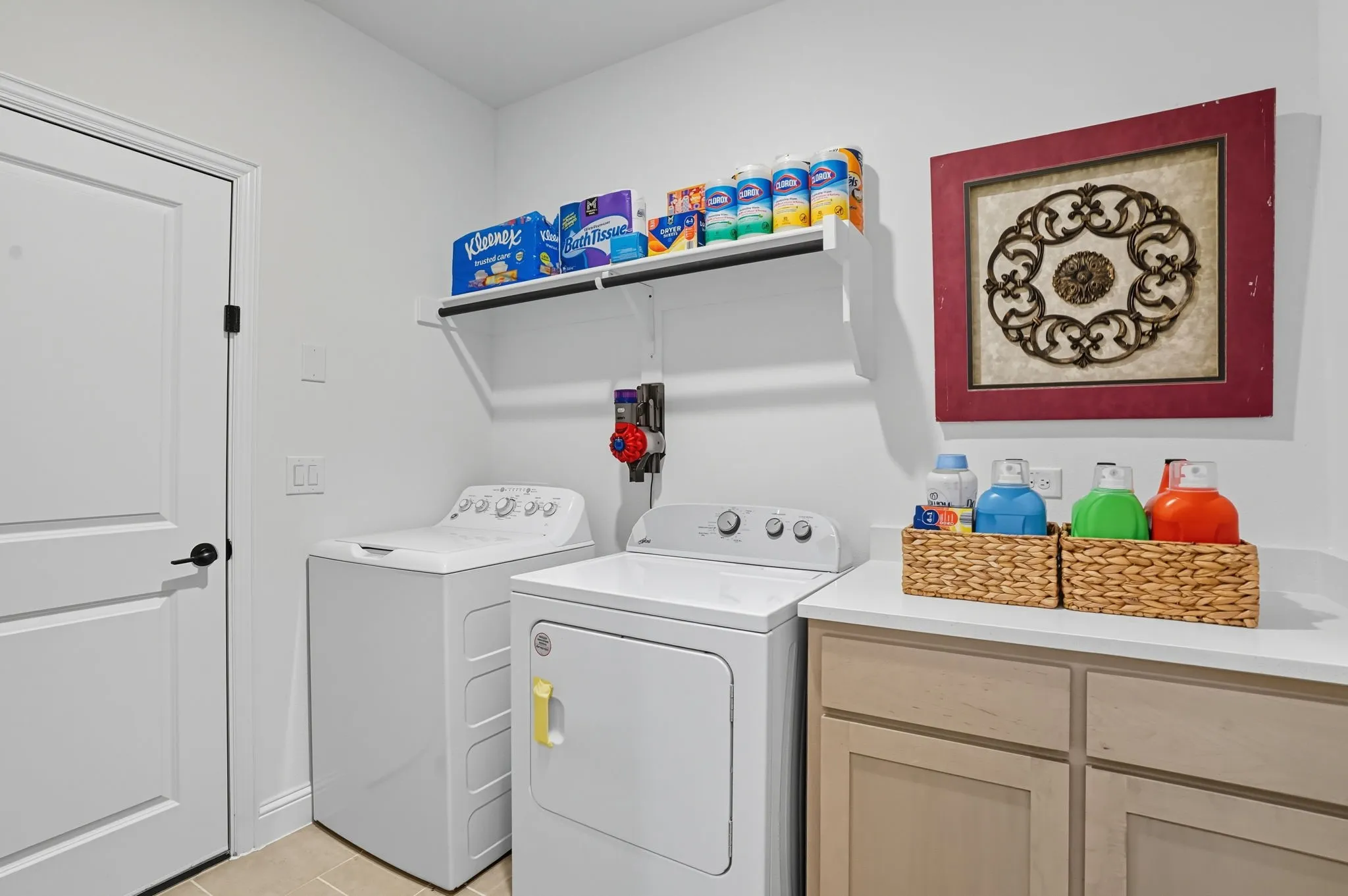 Dedicated laundry area featuring a built-in countertop, light wood-finish cabinetry, and overhead shelving