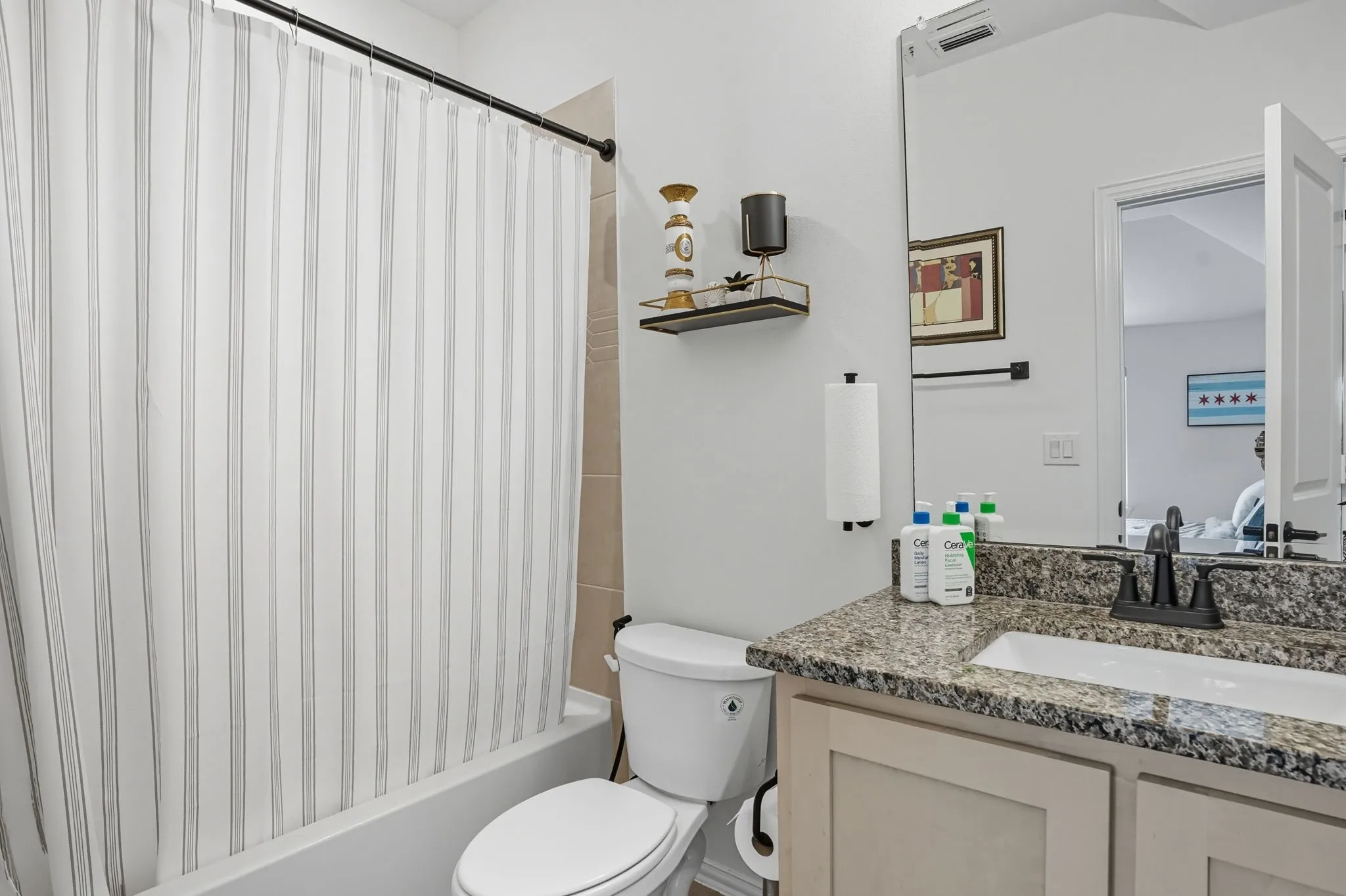 Bathroom featuring a tub/shower combination with a striped shower curtain, light-toned wall tile, a vanity with a stone-finish countertop, an undermount sink, and dark-finish fixtures