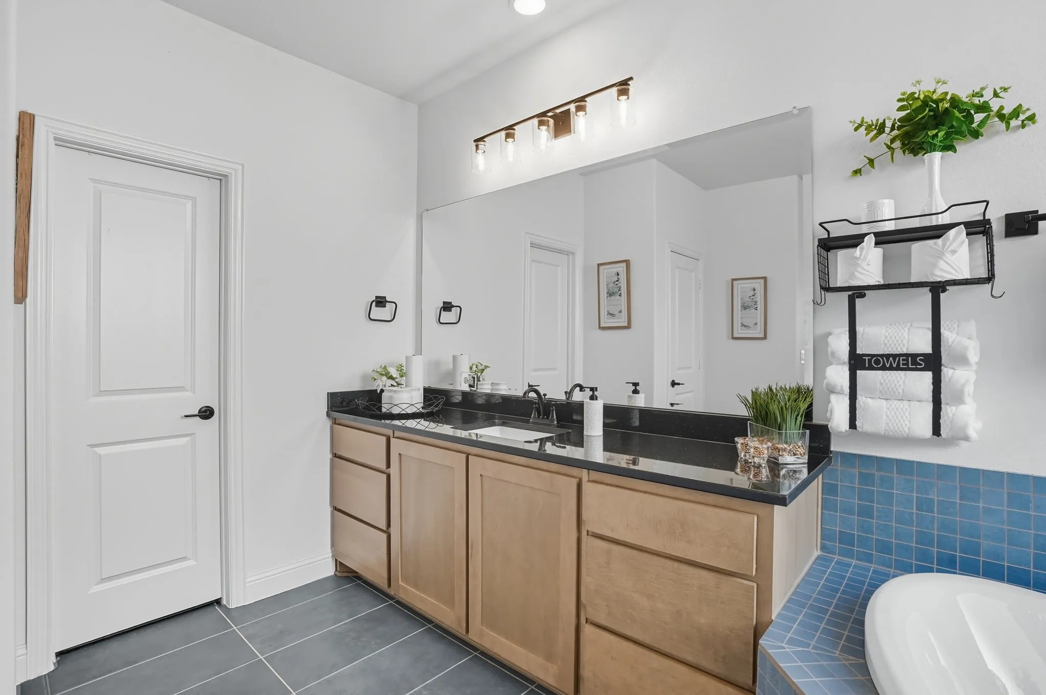 Bathroom vanity with a dark countertop, light wood-finish cabinetry, and a large mirror