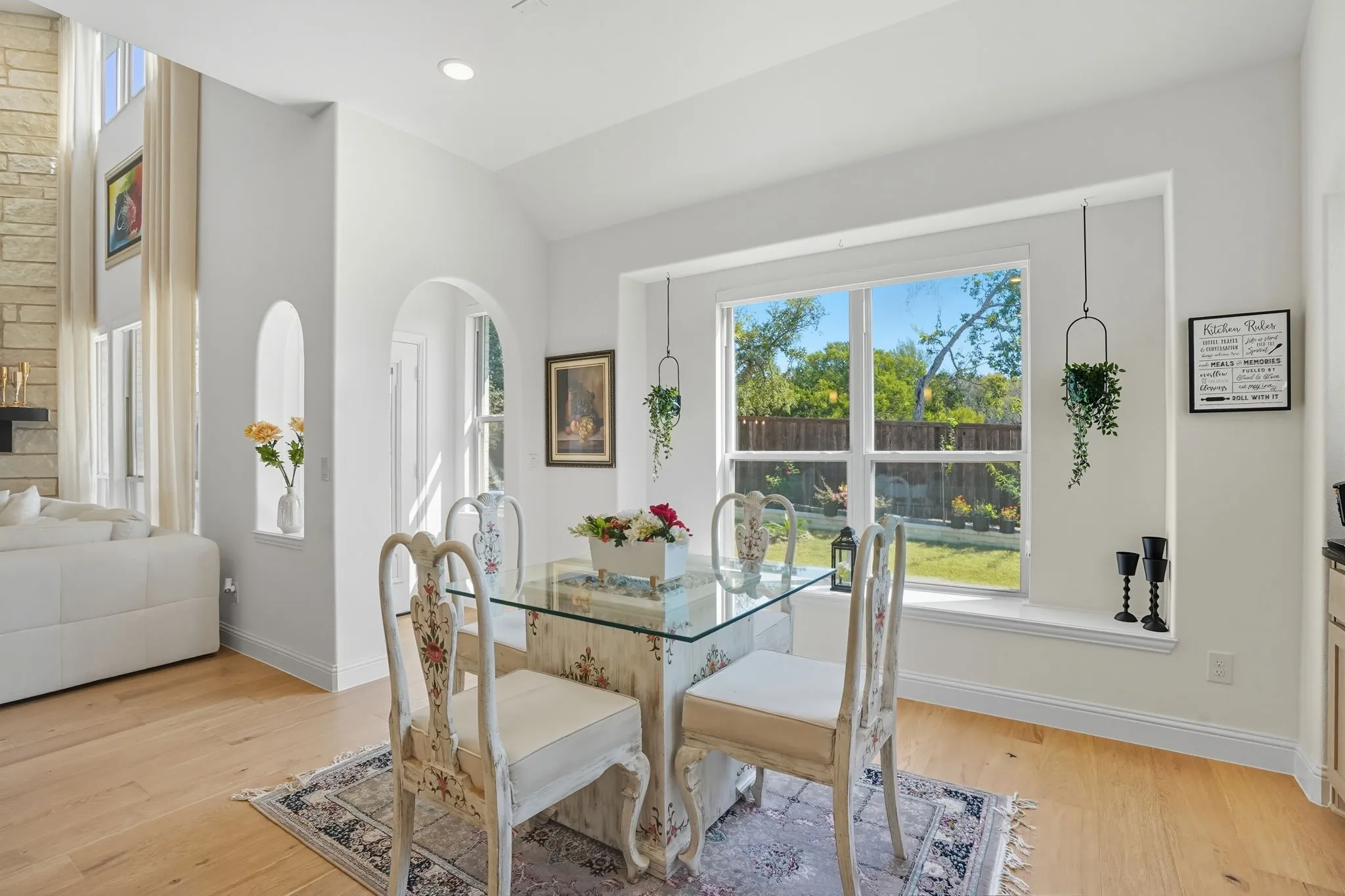 Dining area with hardwood flooring, a large window overlooking the backyard, vaulted ceiling, and an arched entryway