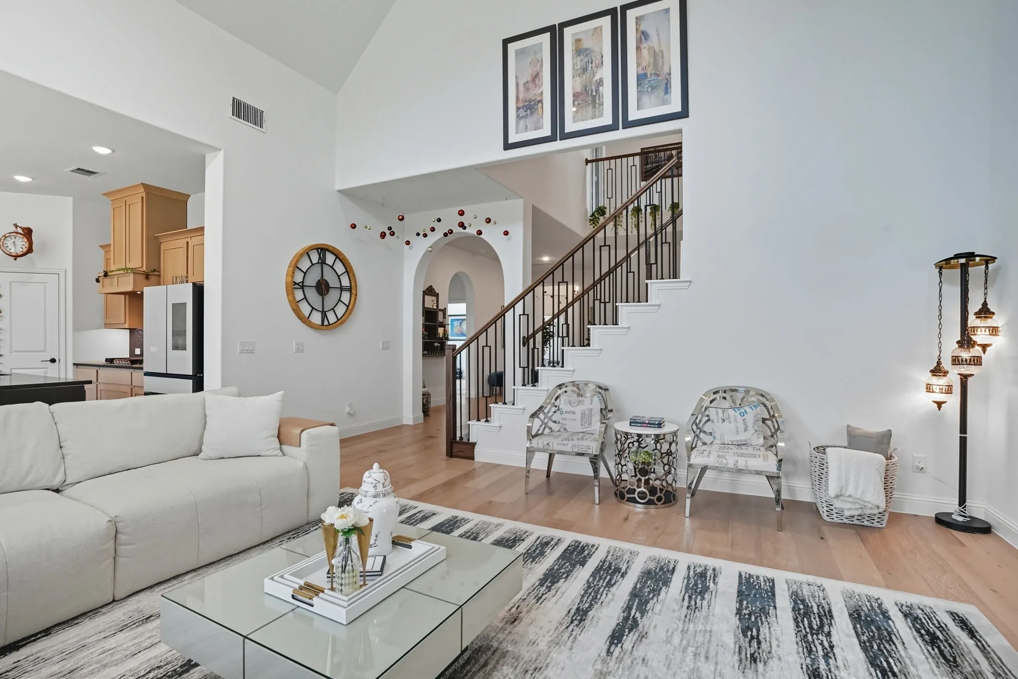 Two-story living area featuring wood-finish flooring, a grand staircase with wrought iron balusters, vaulted ceilings, and an arched doorway