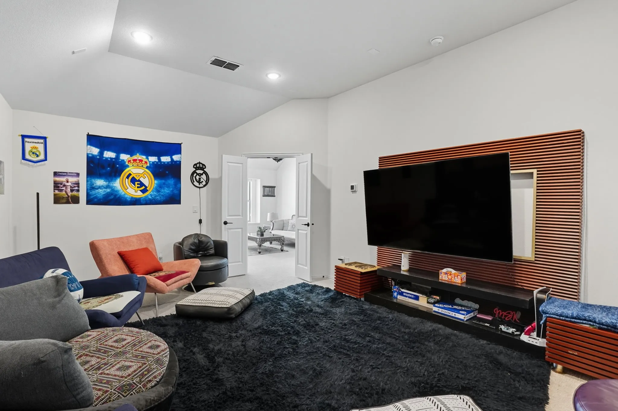 Spacious room with a vaulted ceiling and recessed lighting, featuring a contrasting accent wall with horizontal slats and a wall-mounted media console