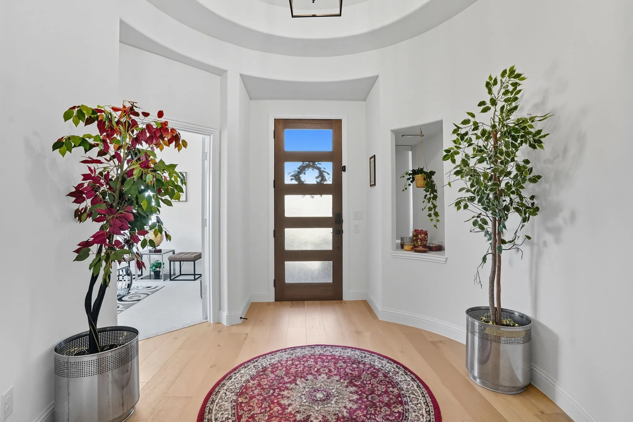Grand entryway featuring a solid wood door with frosted glass panels, light wood-finish flooring, and a curved wall design with a niche