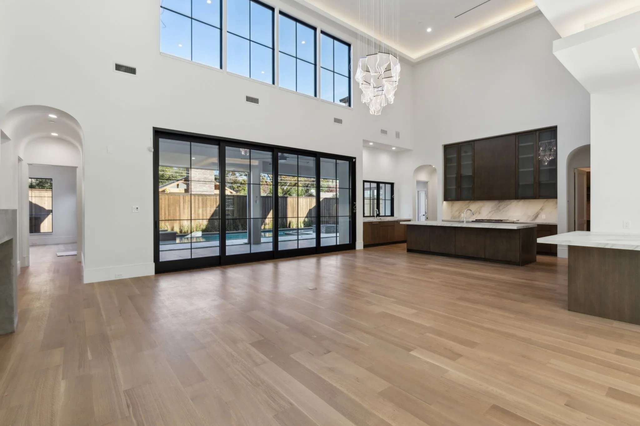 Unfurnished living room with arched walkways, light wood-style floors, plenty of natural light, and a high ceiling