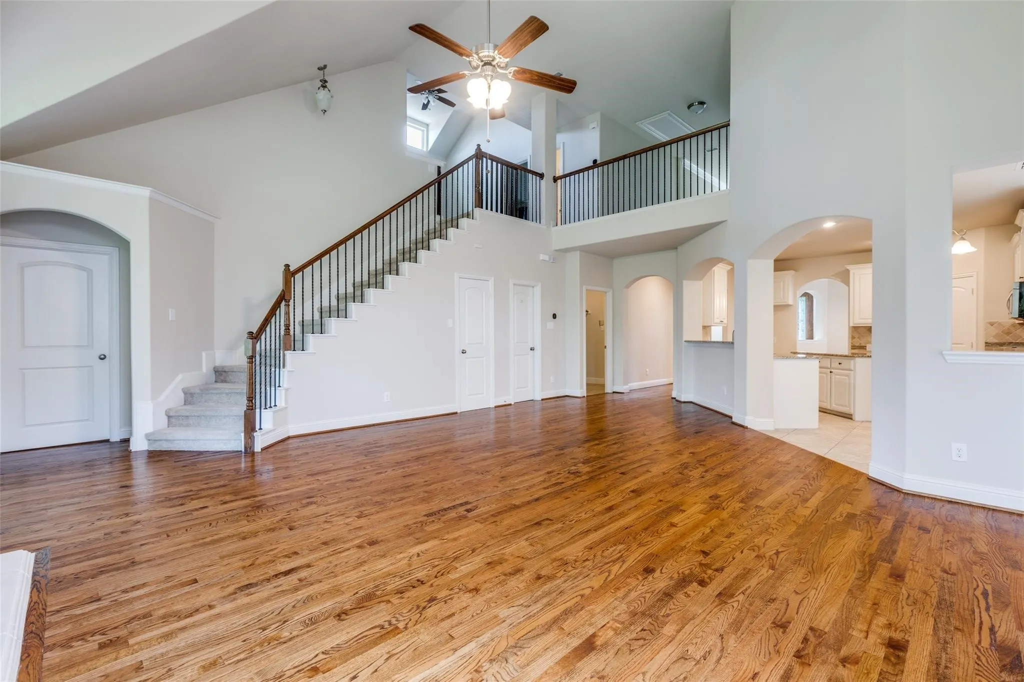 Spacious living area featuring high vaulted ceilings, warm wood-finish flooring, and an open staircase with wrought iron balusters