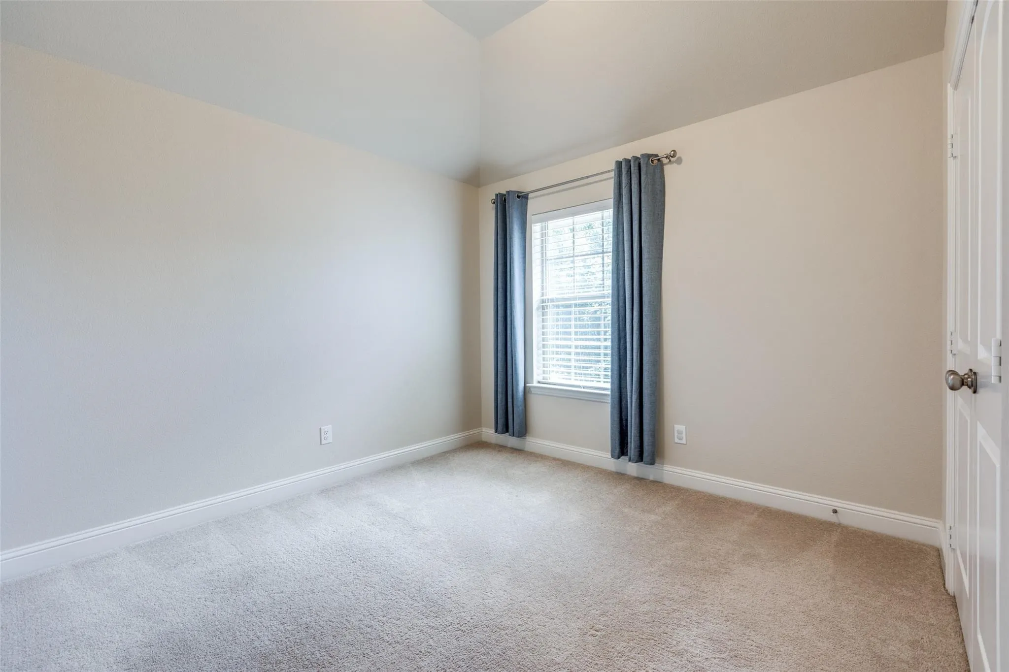 Bedroom featuring a vaulted ceiling, light-toned carpeting, window with blinds, and white trim