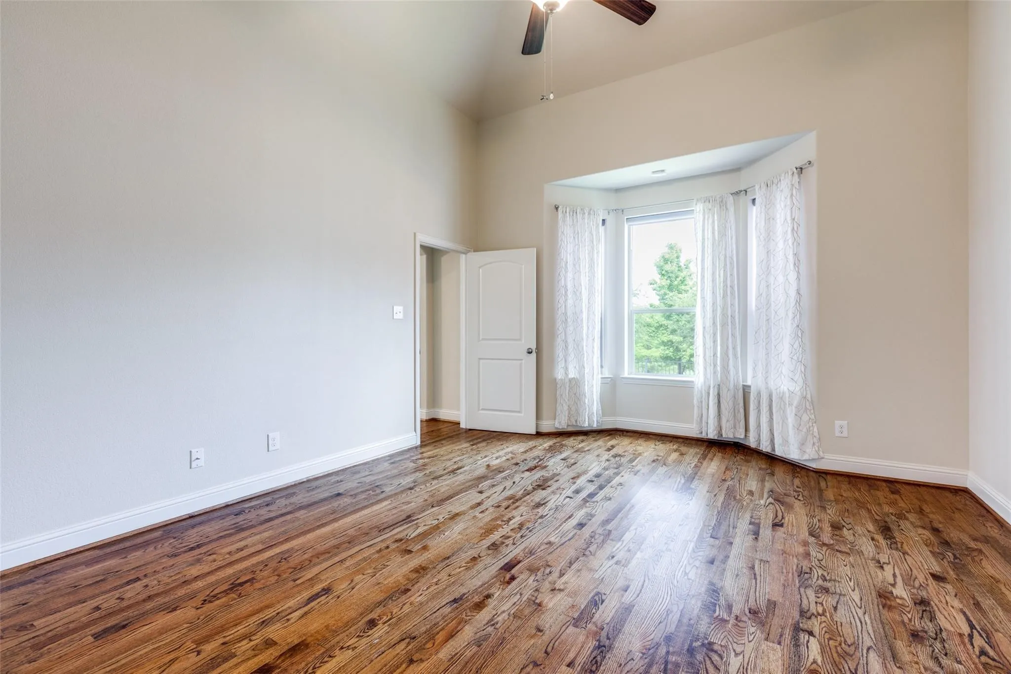 Room featuring wood-finish flooring, a bay window with natural light, vaulted ceilings, and a ceiling fan