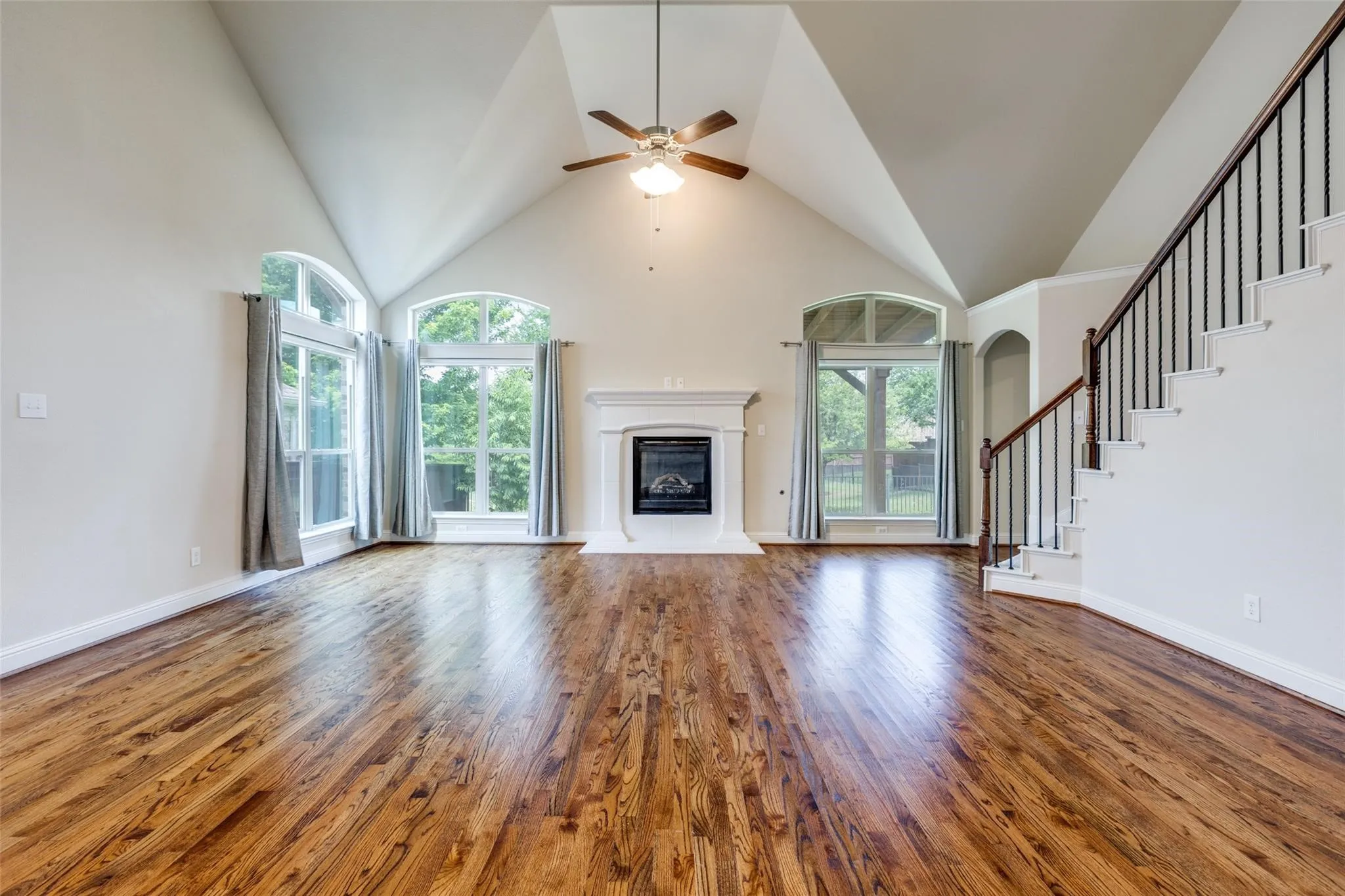 Living area featuring a vaulted ceiling with a ceiling fan, a fireplace with a white mantel, and wood-finish flooring