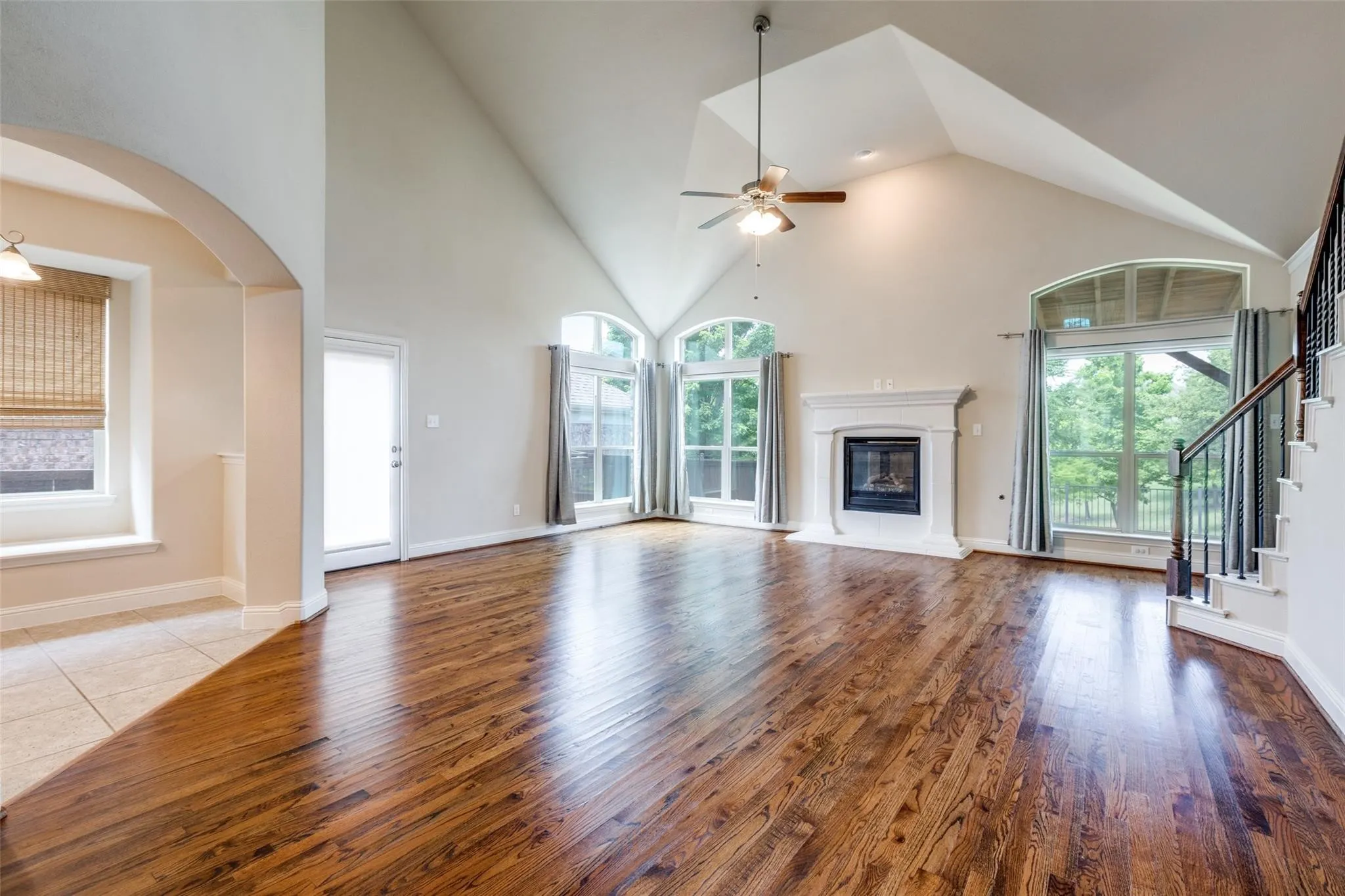 Vaulted living area featuring wood-finish flooring, a ceiling fan, and a fireplace with a white mantel