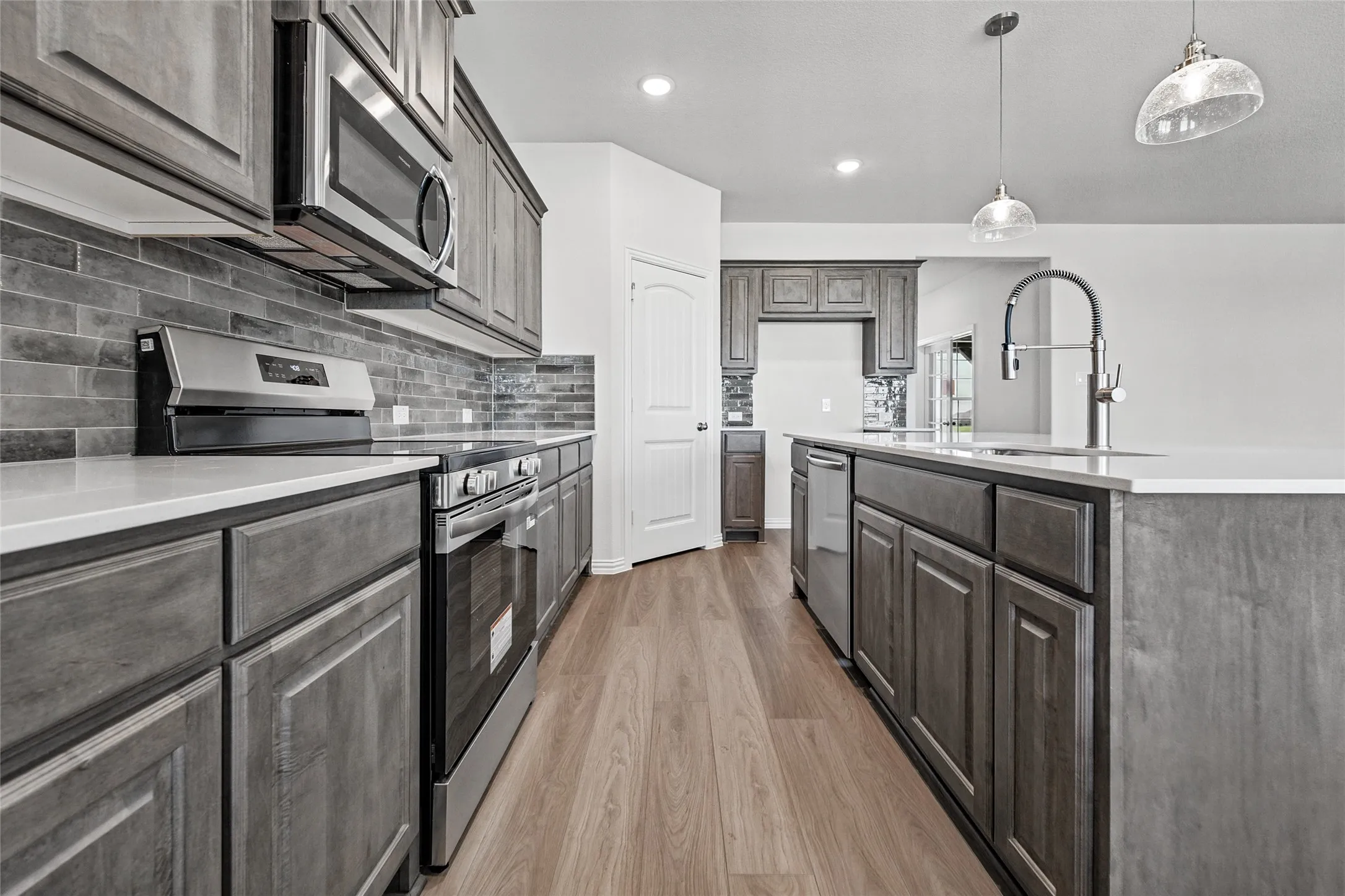 Modern kitchen with wood-finish flooring, stainless steel appliances, white countertops, and a gray tile backsplash