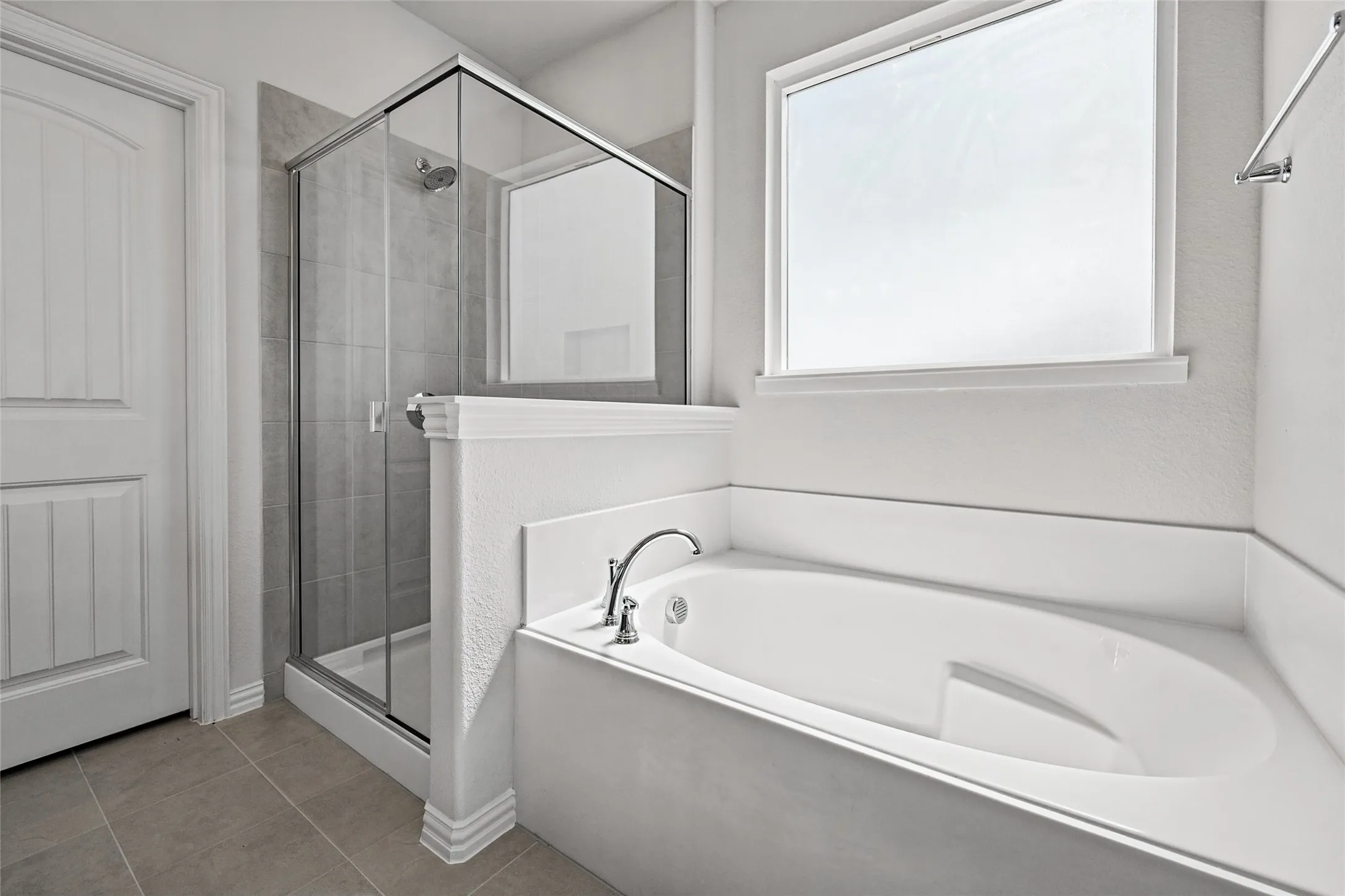 Soaking tub with deck-mounted fixtures, separate glass-enclosed shower with tile surround, and a large window