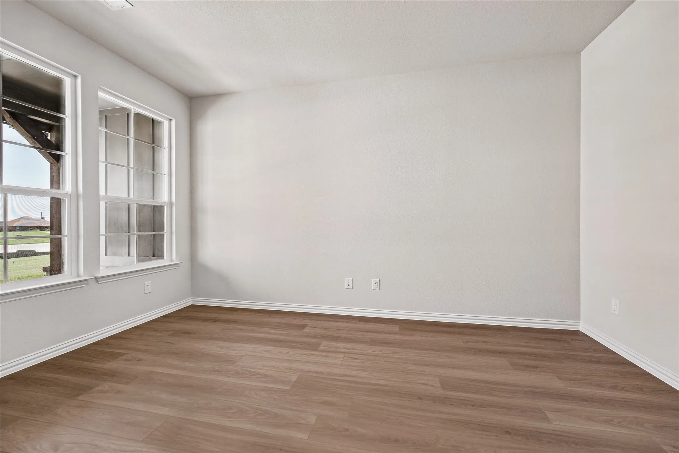 Wood-finish flooring with white baseboards, and two multi-pane windows