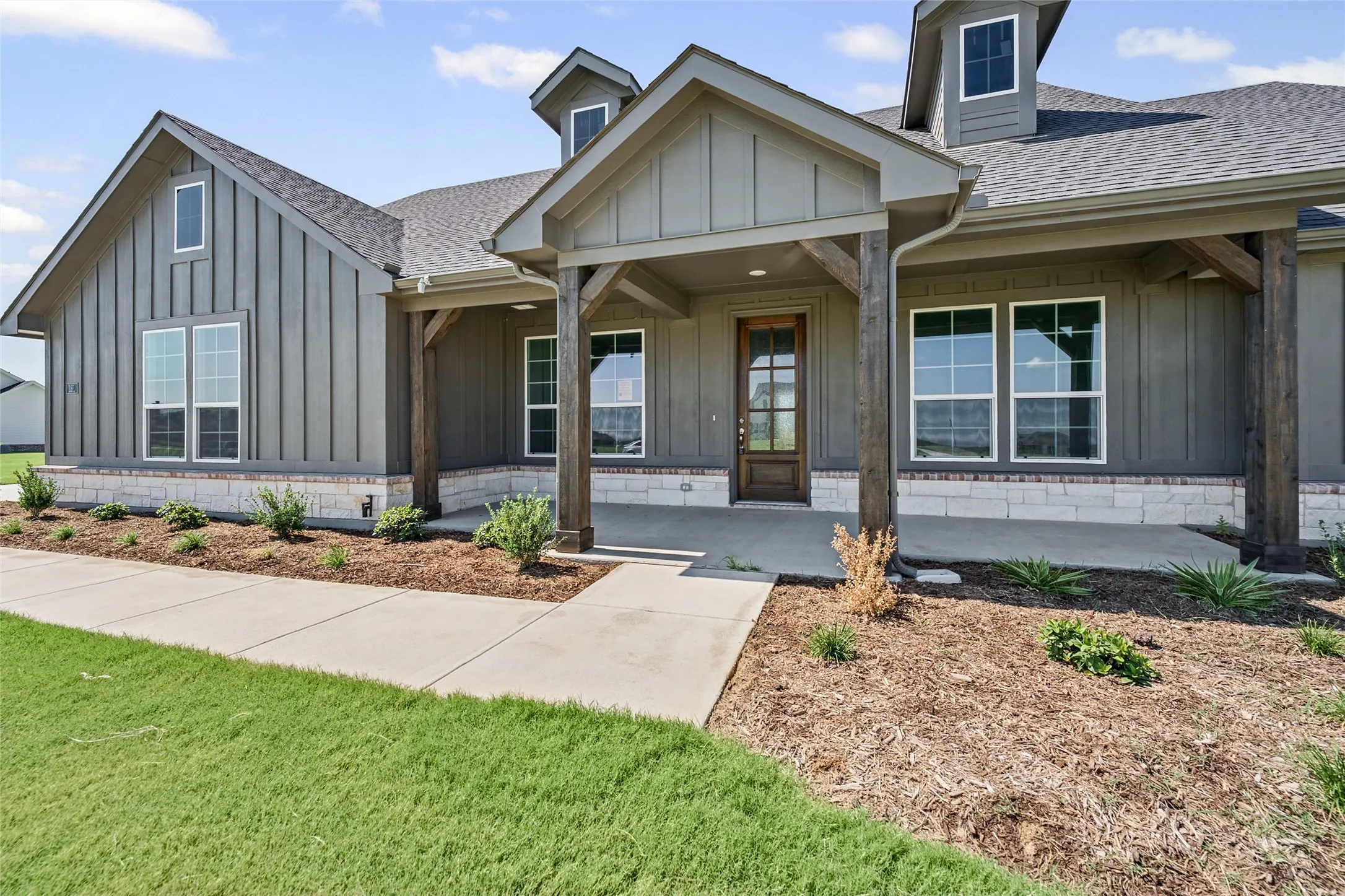 Modern farmhouse exterior with vertical siding, stone skirt, covered porch, exposed beam accents, and dormer windows
