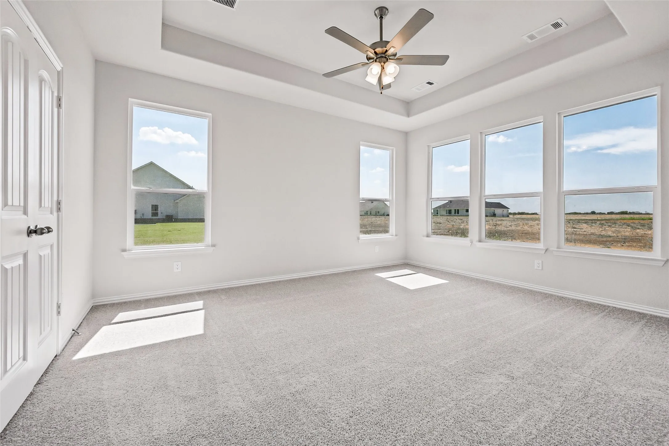 Tray ceiling with a ceiling fan light fixture, white paneled door, and multiple windows