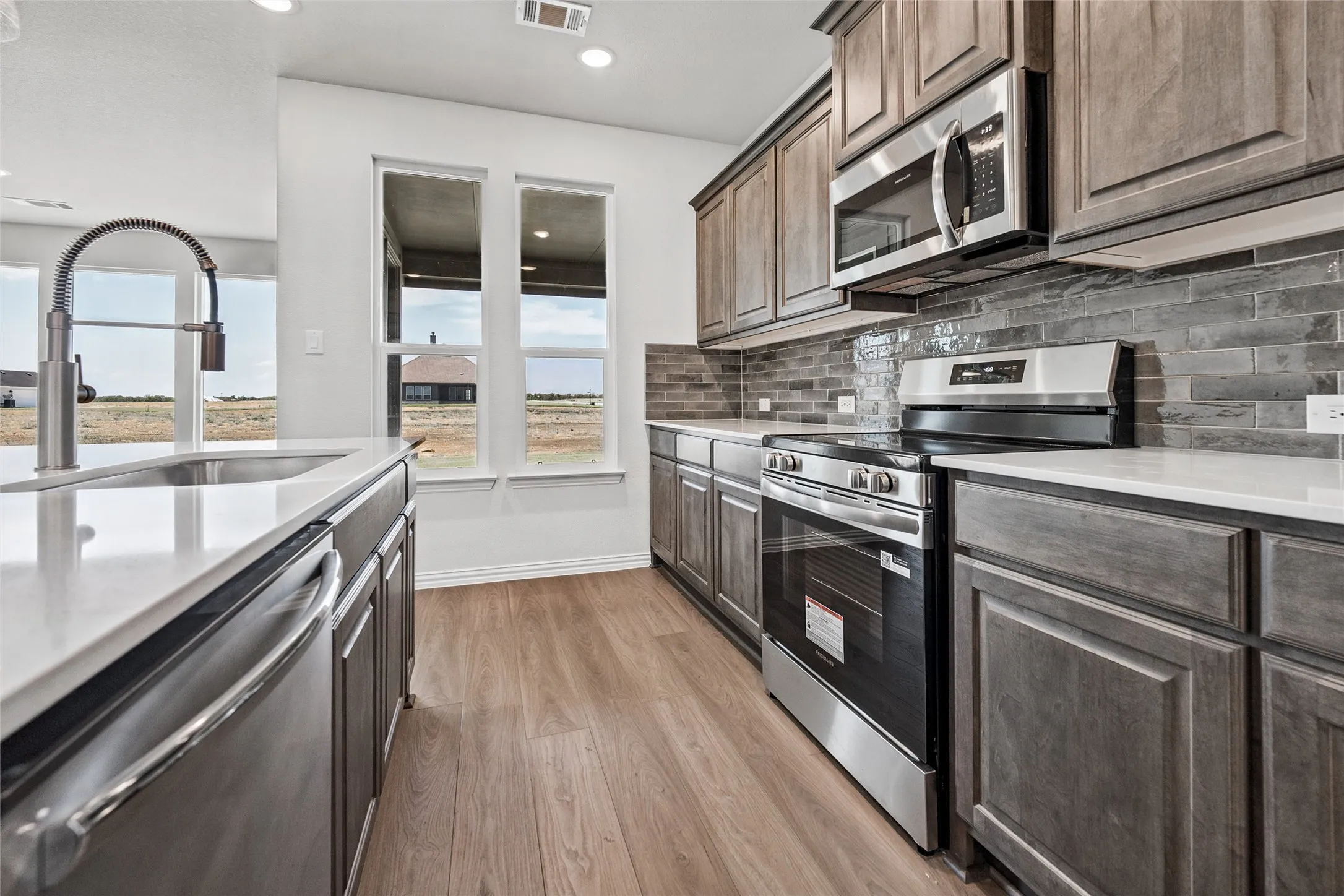 Kitchen featuring wood-finish flooring, white countertops, stainless steel appliances, and a stacked tile backsplash