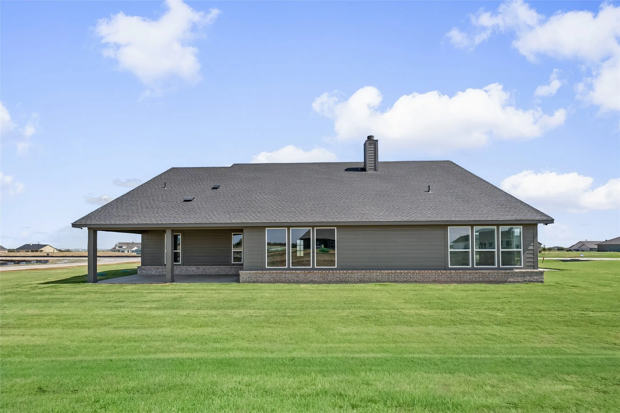 Expansive rear exterior featuring a covered patio, multiple windows, and a brick foundation
