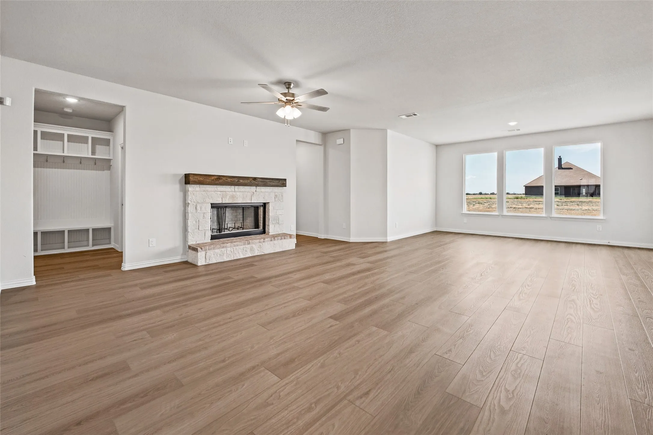 Spacious living area featuring wood-finish flooring, a stone-clad fireplace with a wood mantel, a ceiling fan, and a built-in storage bench with shelving
