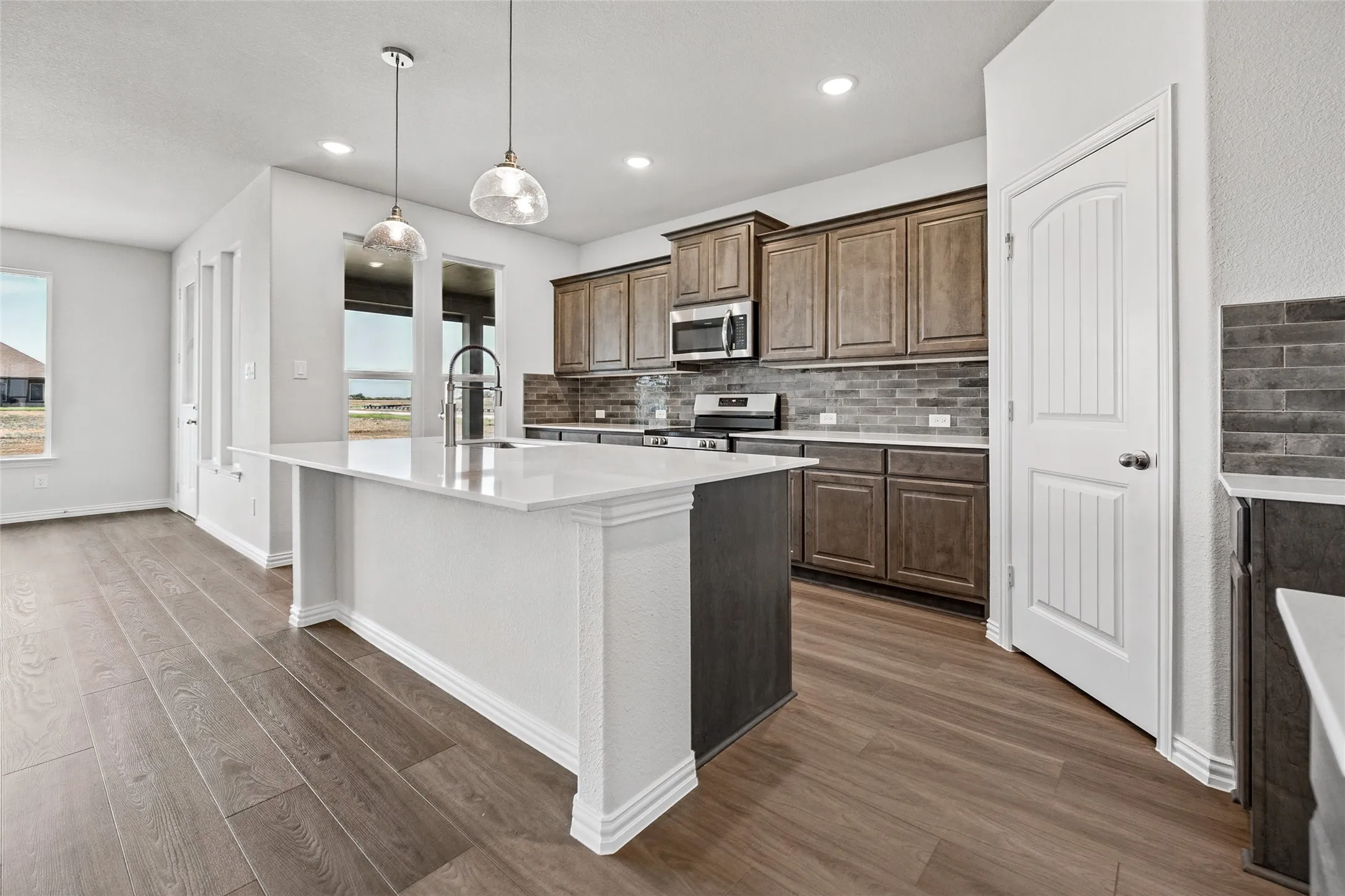 Kitchen featuring an expansive island with a white countertop, wood-finish flooring, recessed lighting, and a subway tile backsplash