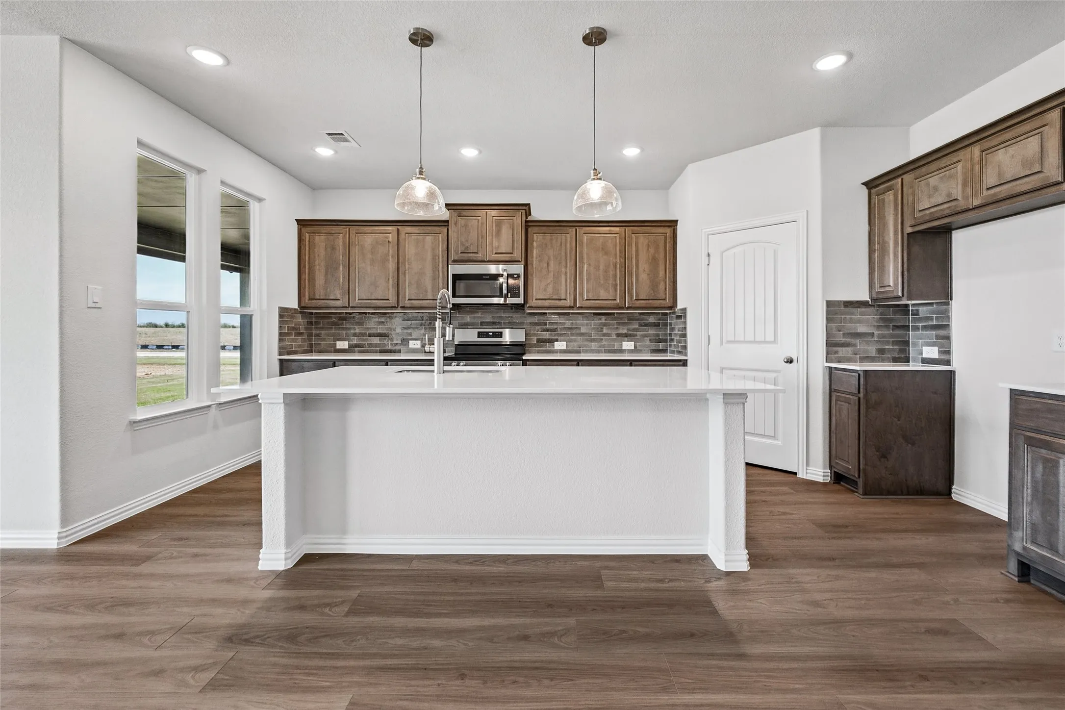 Spacious kitchen featuring a large island with quartz countertops, wood-finish flooring, recessed lighting, and upper and lower cabinetry