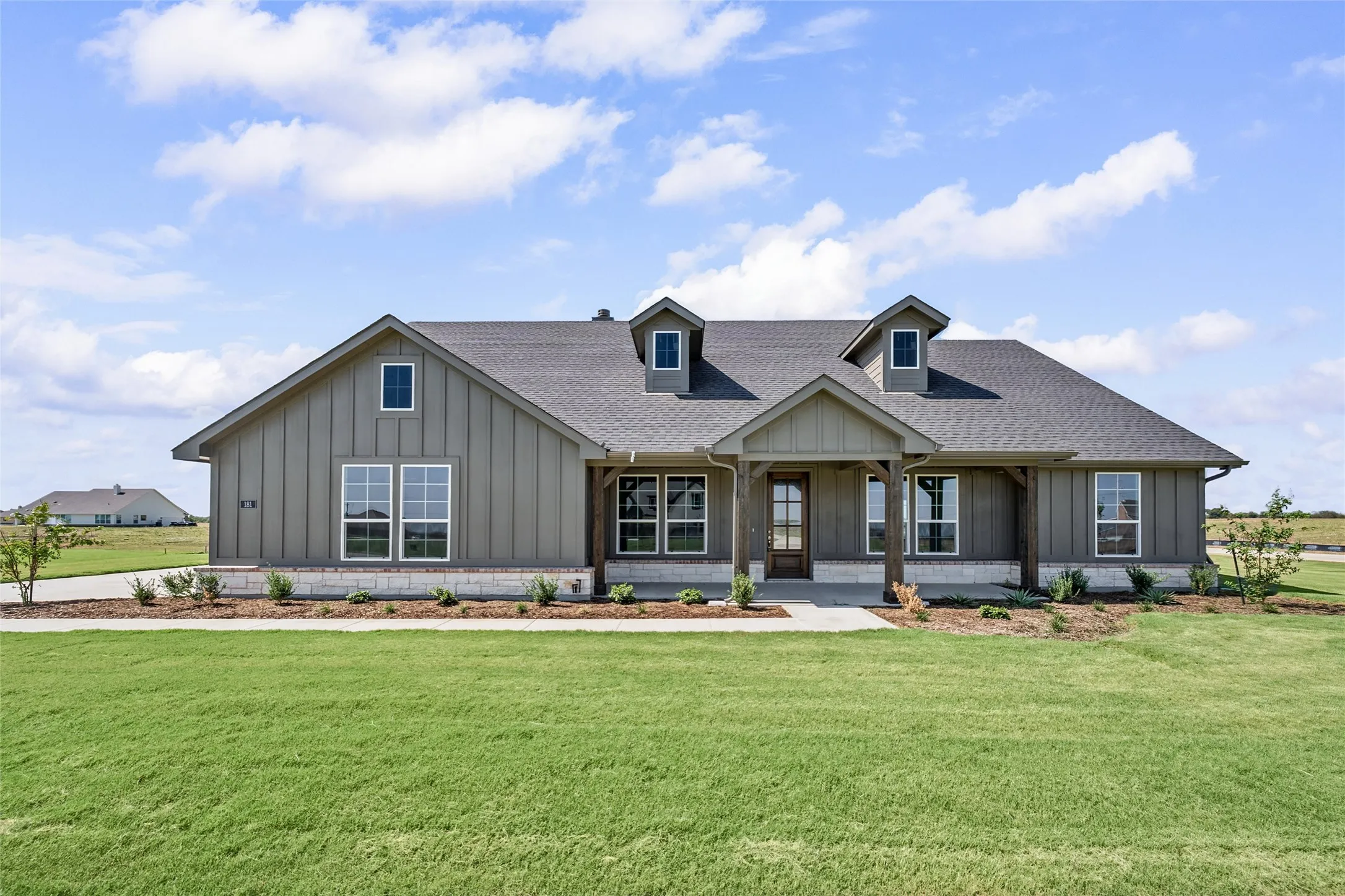 Modern farmhouse exterior featuring board and batten siding, stone accents, a covered entry porch with wood-finish columns, a dark shingle roof, and multiple dormer windows