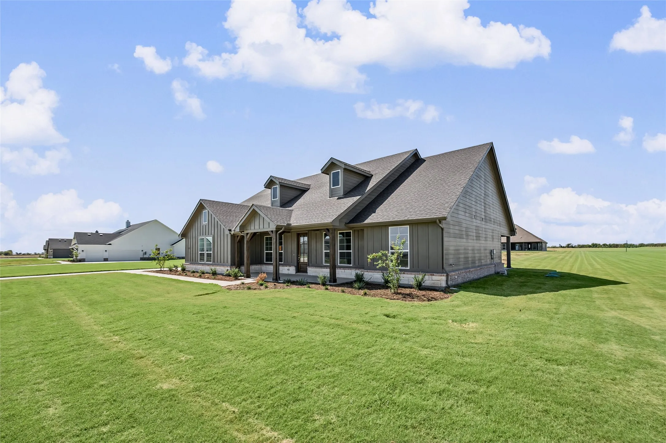 Contemporary farmhouse exterior featuring dormer windows, a covered front porch, vertical siding, a stone base, and a gabled roof
