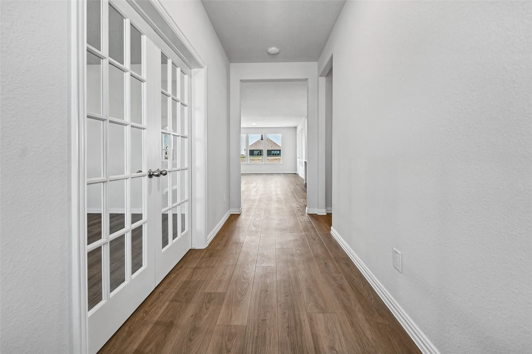 Hallway featuring rich wood-finish flooring, white painted French doors with multi-pane glass panels, and clean white walls with recessed lighting throughout