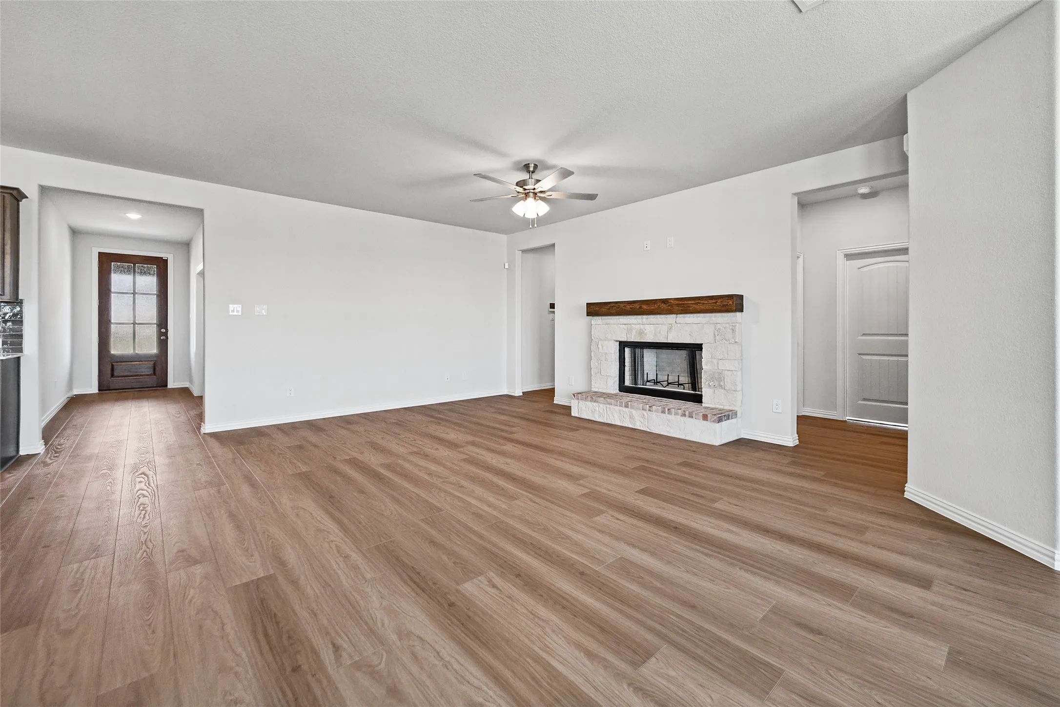 Wood-finish flooring throughout, white walls, stone-tiled fireplace with wood mantel, ceiling fan, and paneled interior doors